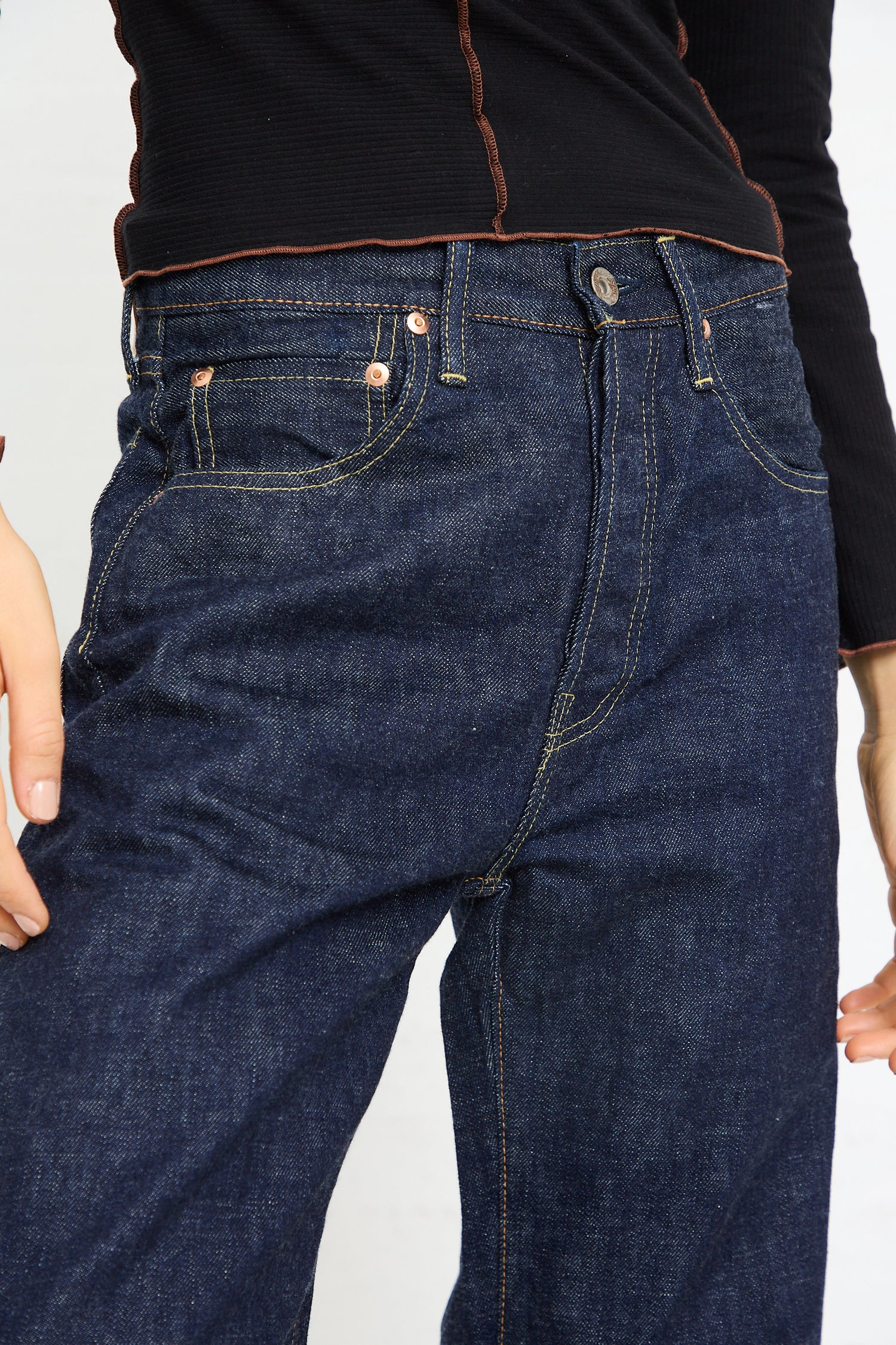 Close-up of a person wearing blue Chimala 13.5 oz. Selvedge Denim Straight Cut in Rinse jeans and a black top.