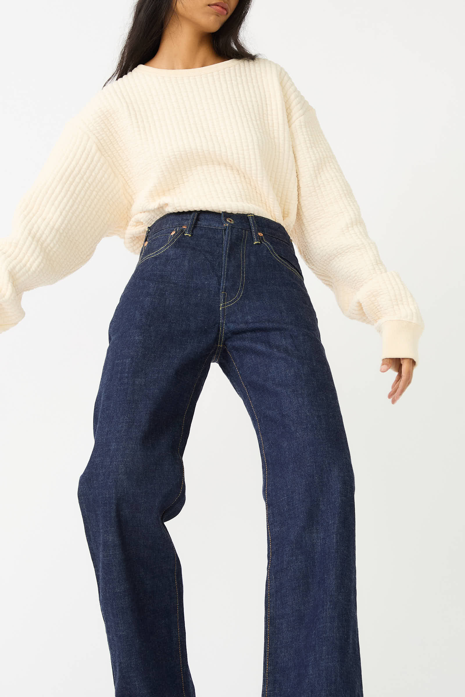 A person is wearing a cream-colored, long-sleeve knit sweater and Chimala's 13.5 oz Selvedge Denim Straight Cut jeans in Rinse.