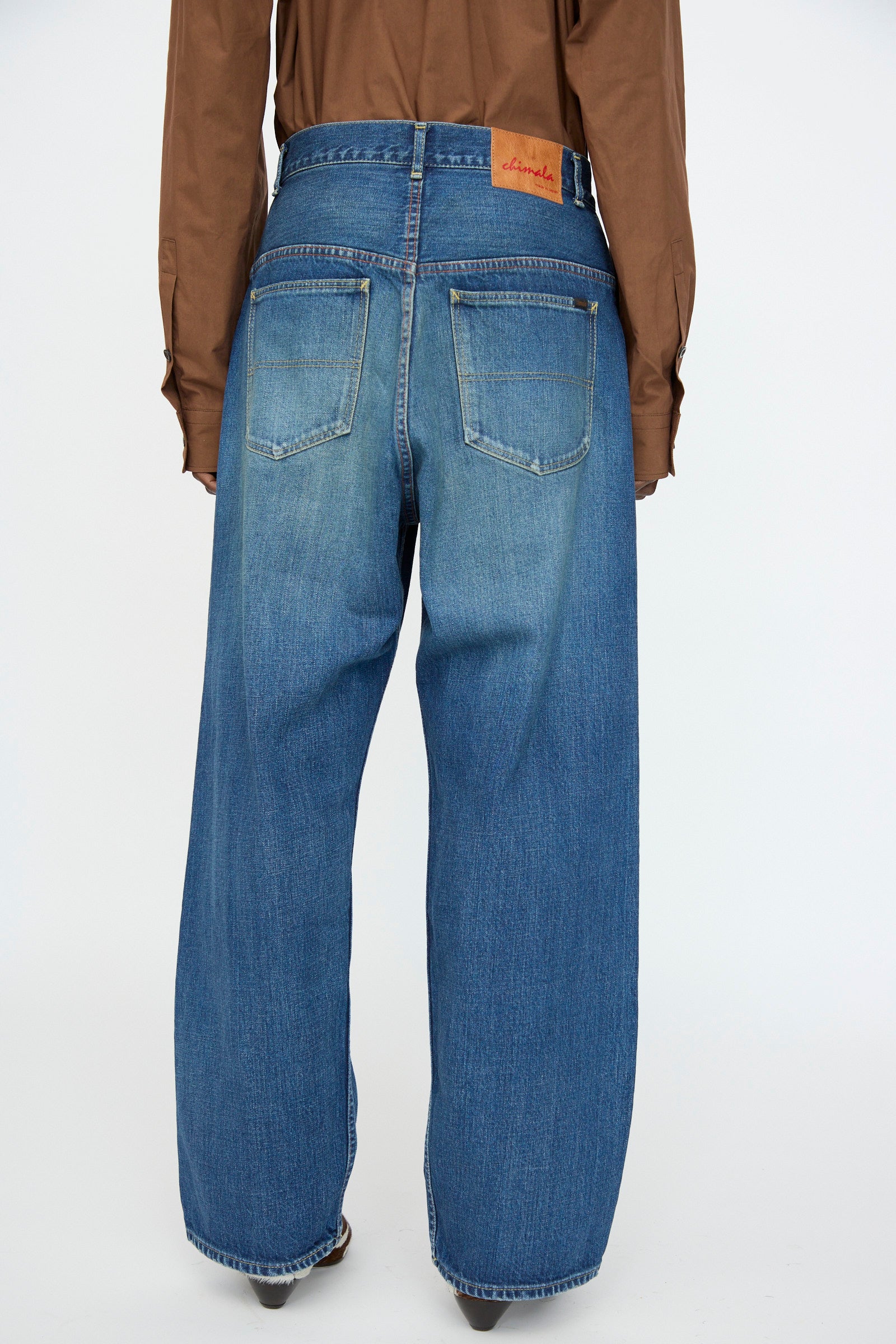 A person shown from the back against a plain background wears a brown long-sleeve shirt and Chimala’s 13oz. Selvedge Denim Ranch Pants in Dark Wash, styled in a relaxed wide-leg fit. 