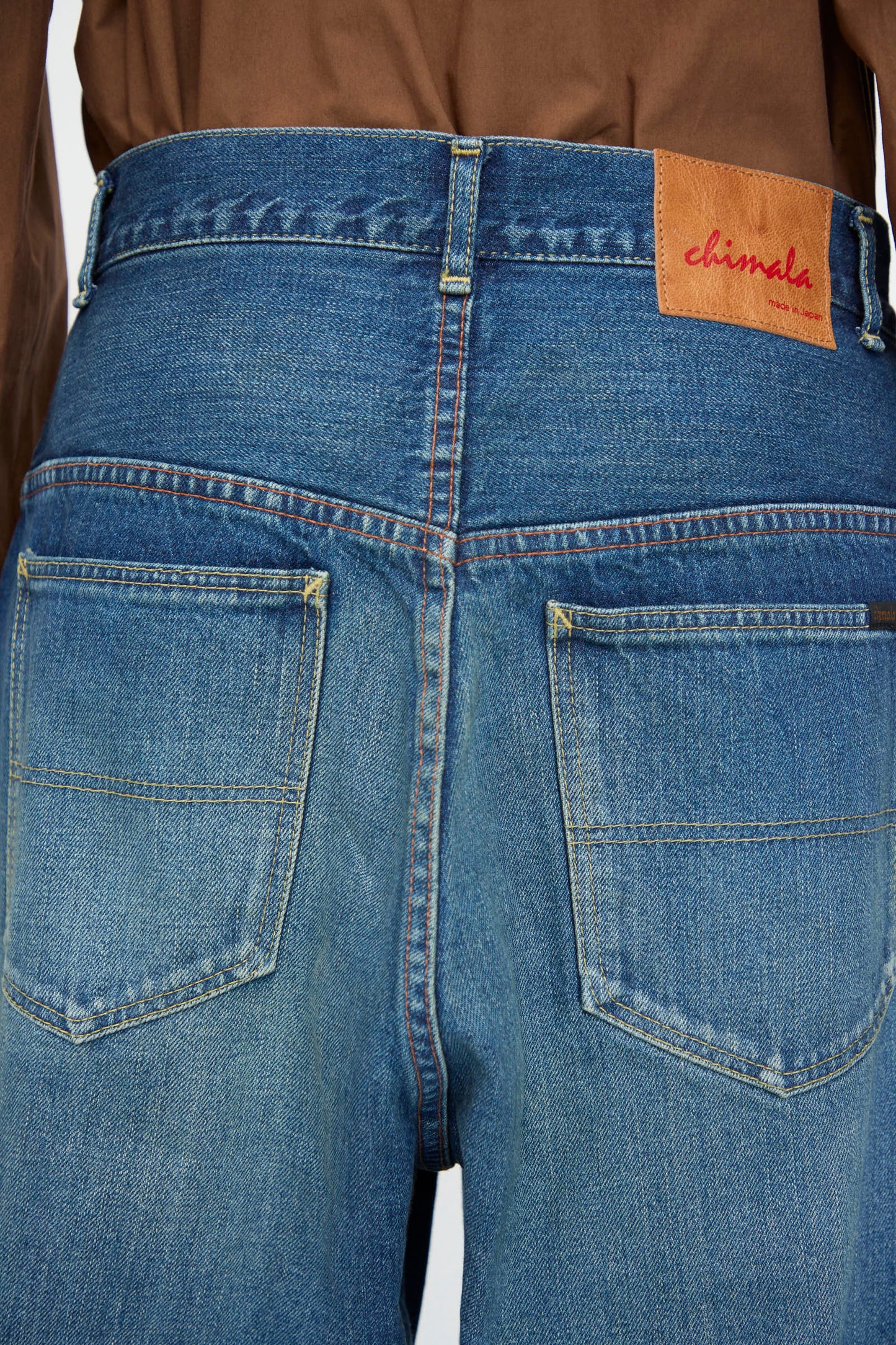Close-up of the back of Chimala's 13oz. Selvedge Denim Ranch Pants in Dark Wash, made from distressed selvedge denim, featuring two back pockets and a brown leather "chimala" patch on the waistband.