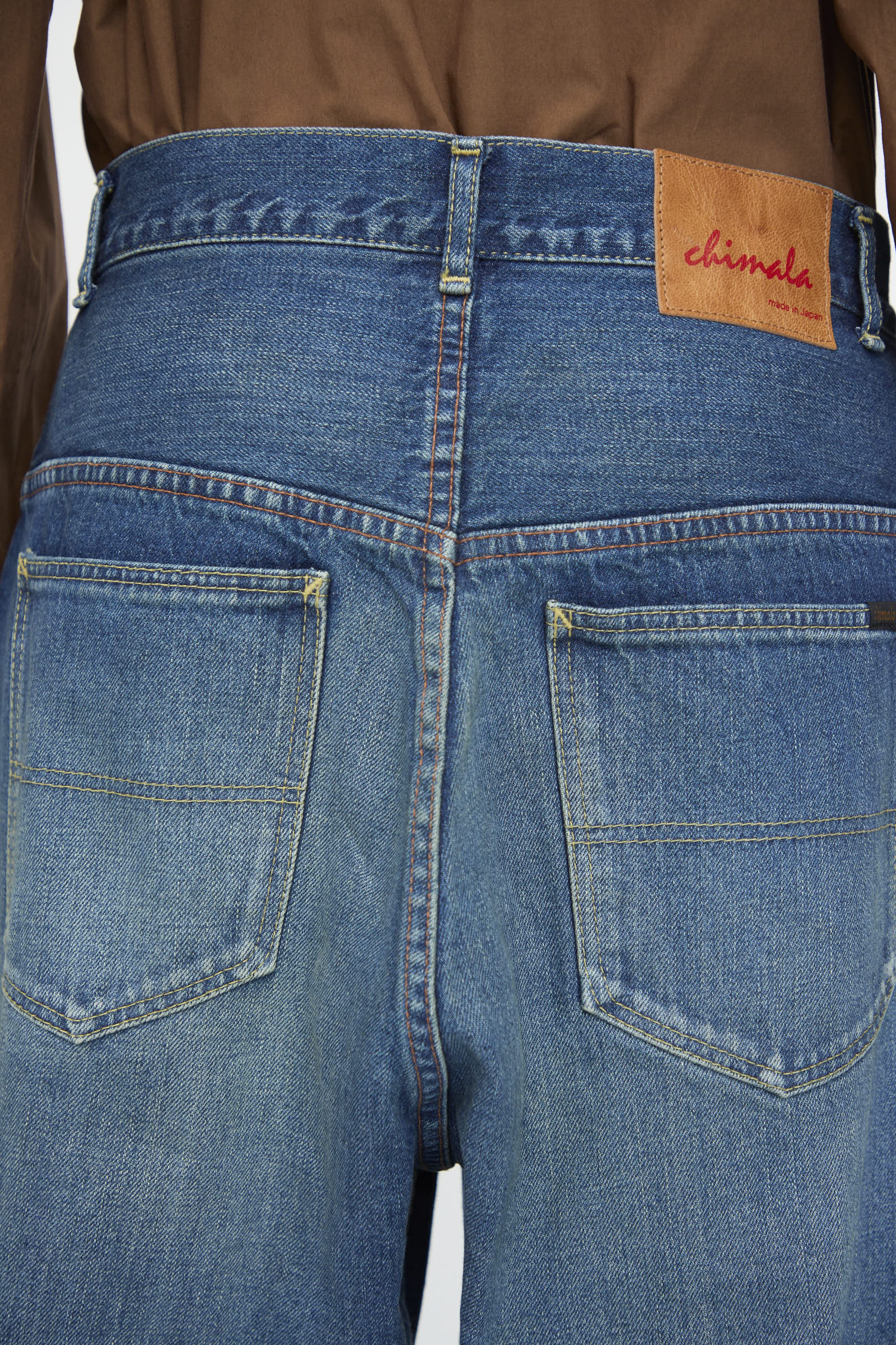 Close-up of the back of Chimala's 13oz. Selvedge Denim Ranch Pants in Dark Wash, made from distressed selvedge denim, featuring two back pockets and a brown leather "chimala" patch on the waistband.