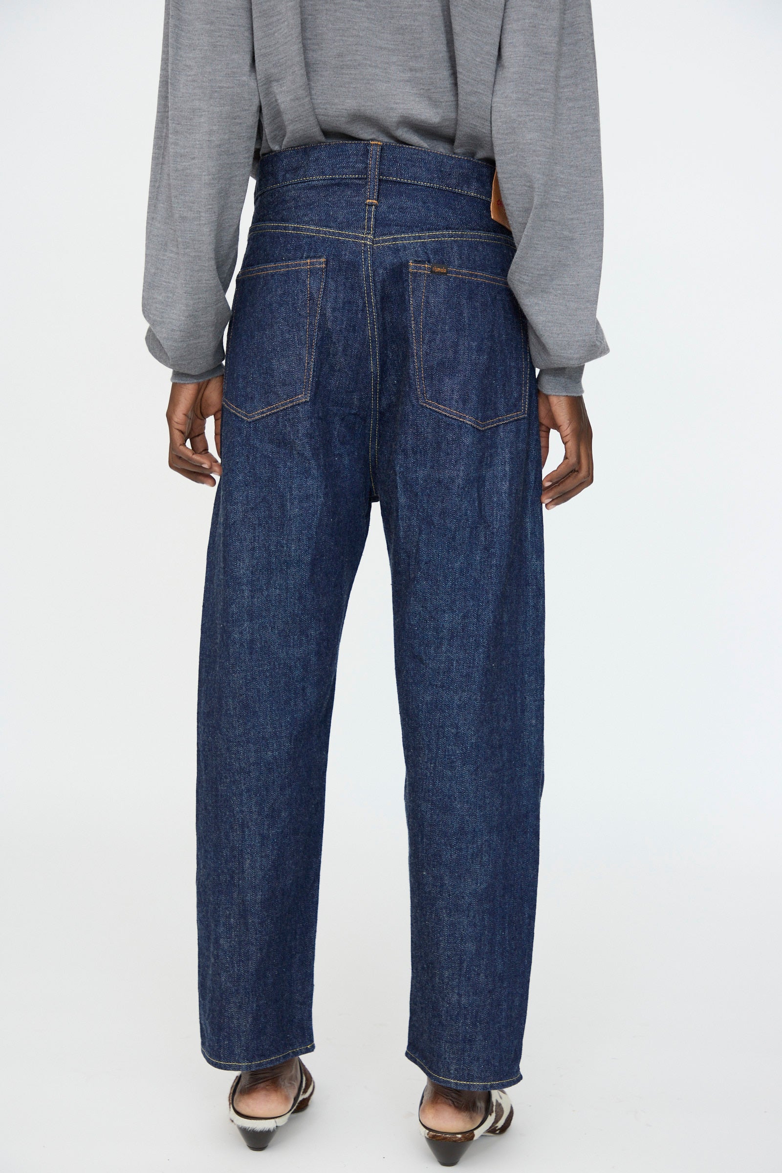 Person wearing a gray long-sleeve shirt and Chimala 13oz. Selvedge Denim Wide Tapered Cut in Rinse jeans, viewed from the back, standing on a light background.