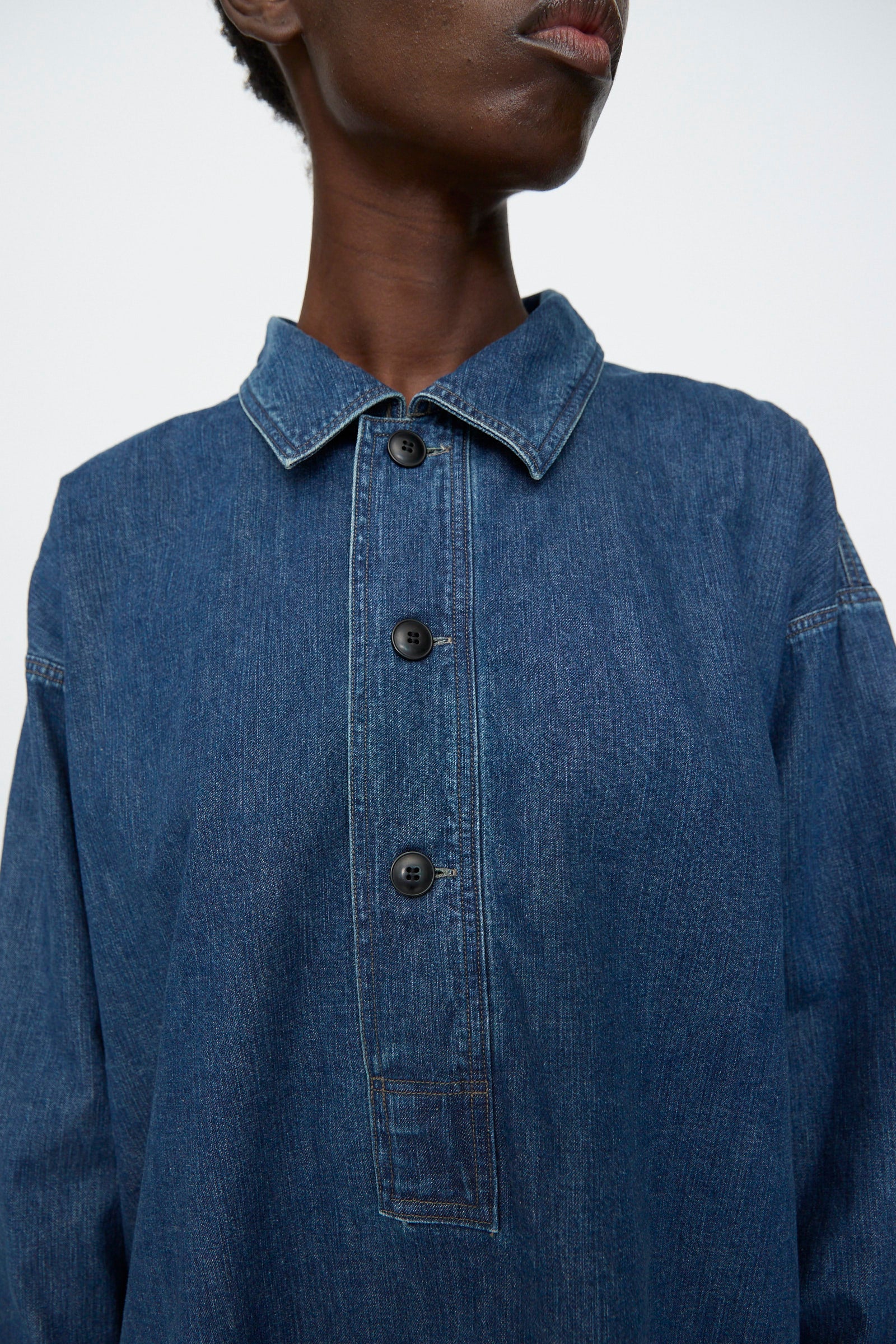 A person wears the Chimala 8oz. Denim US Navydeck Shirt in Indigo—an oversized, collared shirt with three black buttons—photographed from the shoulders up.