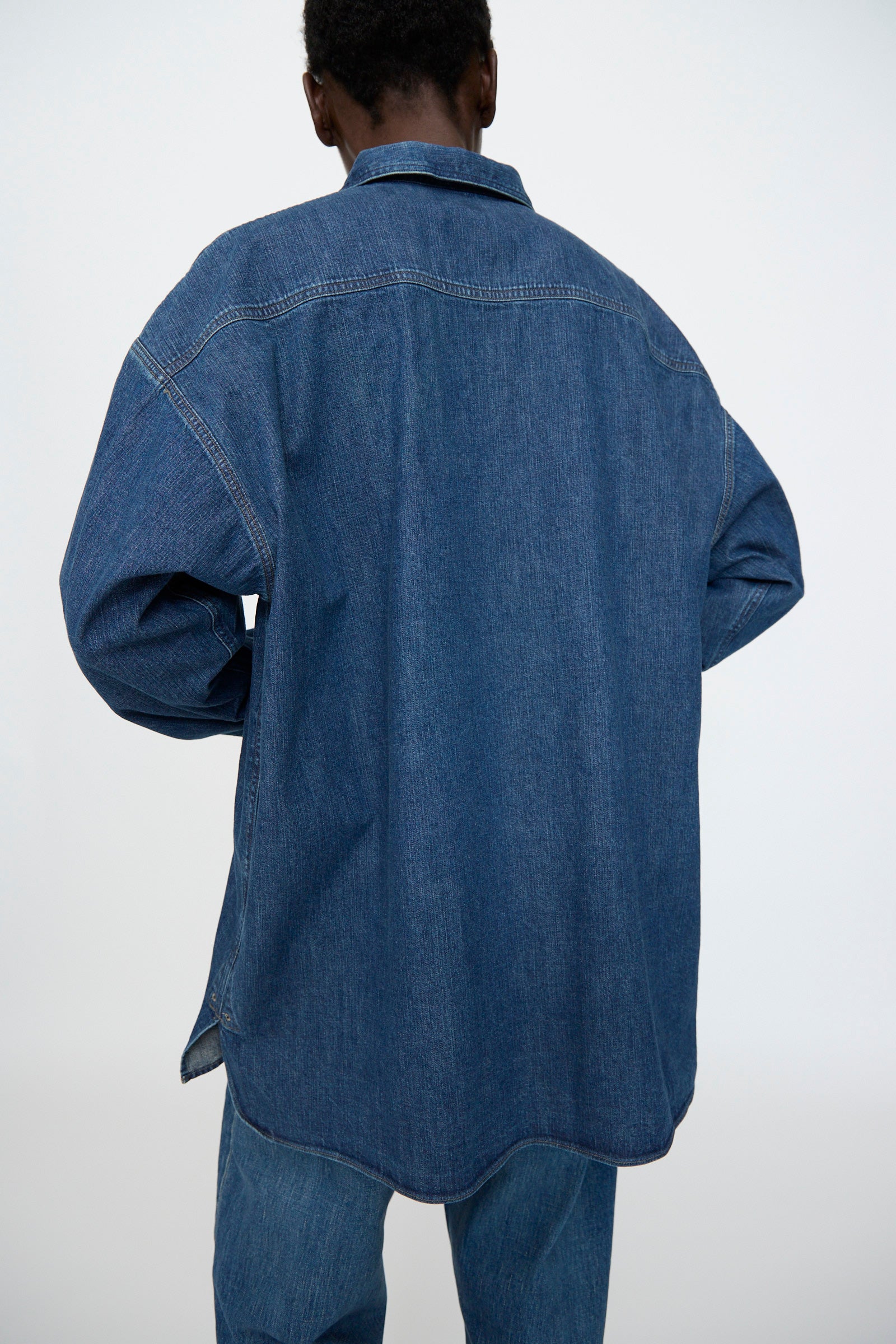 A person is shown from behind wearing the Chimala 8oz. Denim US Navydeck Shirt in Indigo with blue jeans, set against a plain light background.
