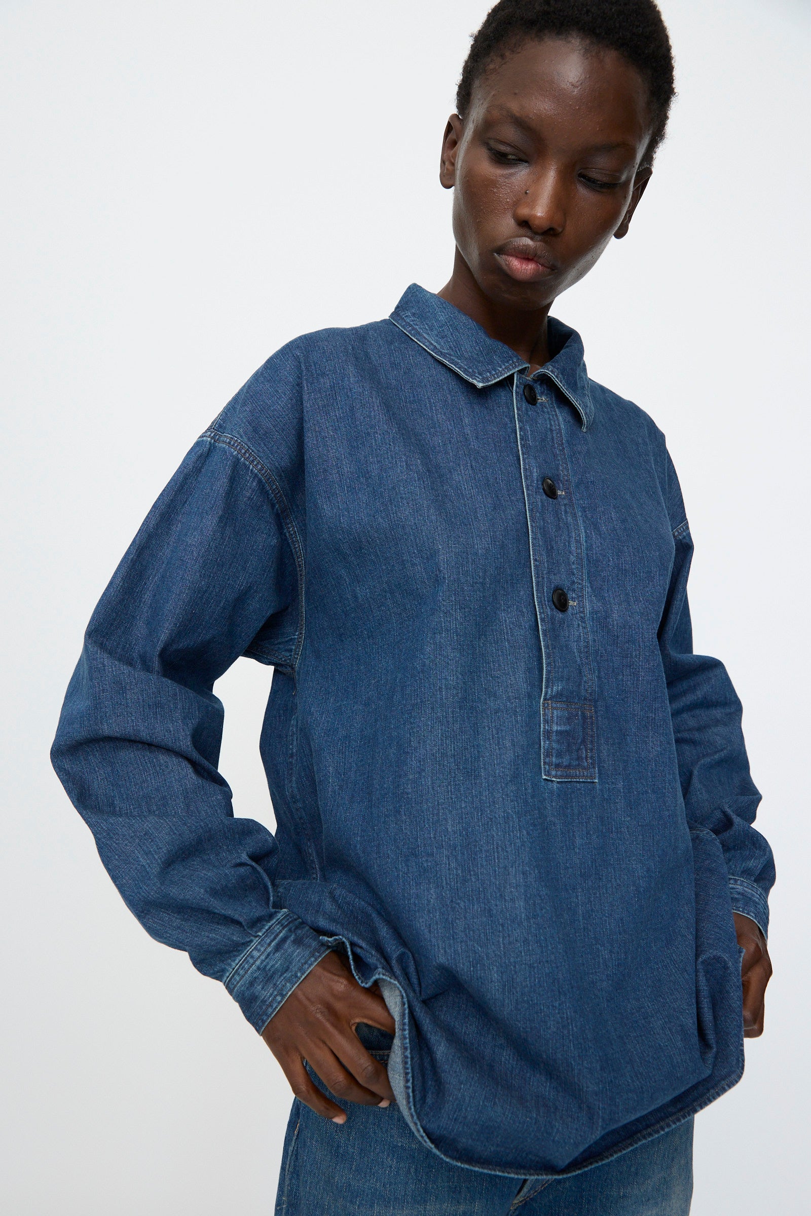 A person wearing the Chimala 8oz. Denim US Navydeck Shirt in Indigo with blue jeans stands against a plain light background, showcasing this classic, premium-quality Japanese-made piece.