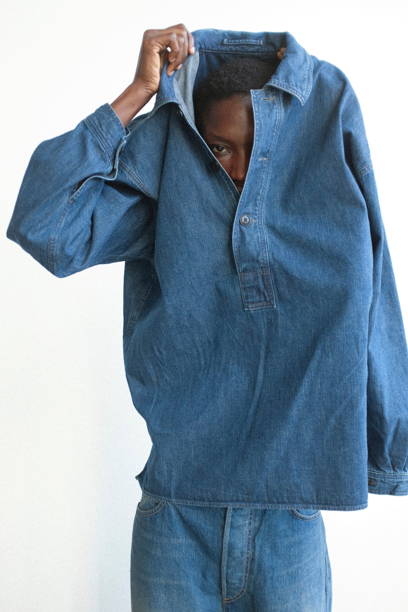 Person wearing a blue denim shirt and pants against a white background