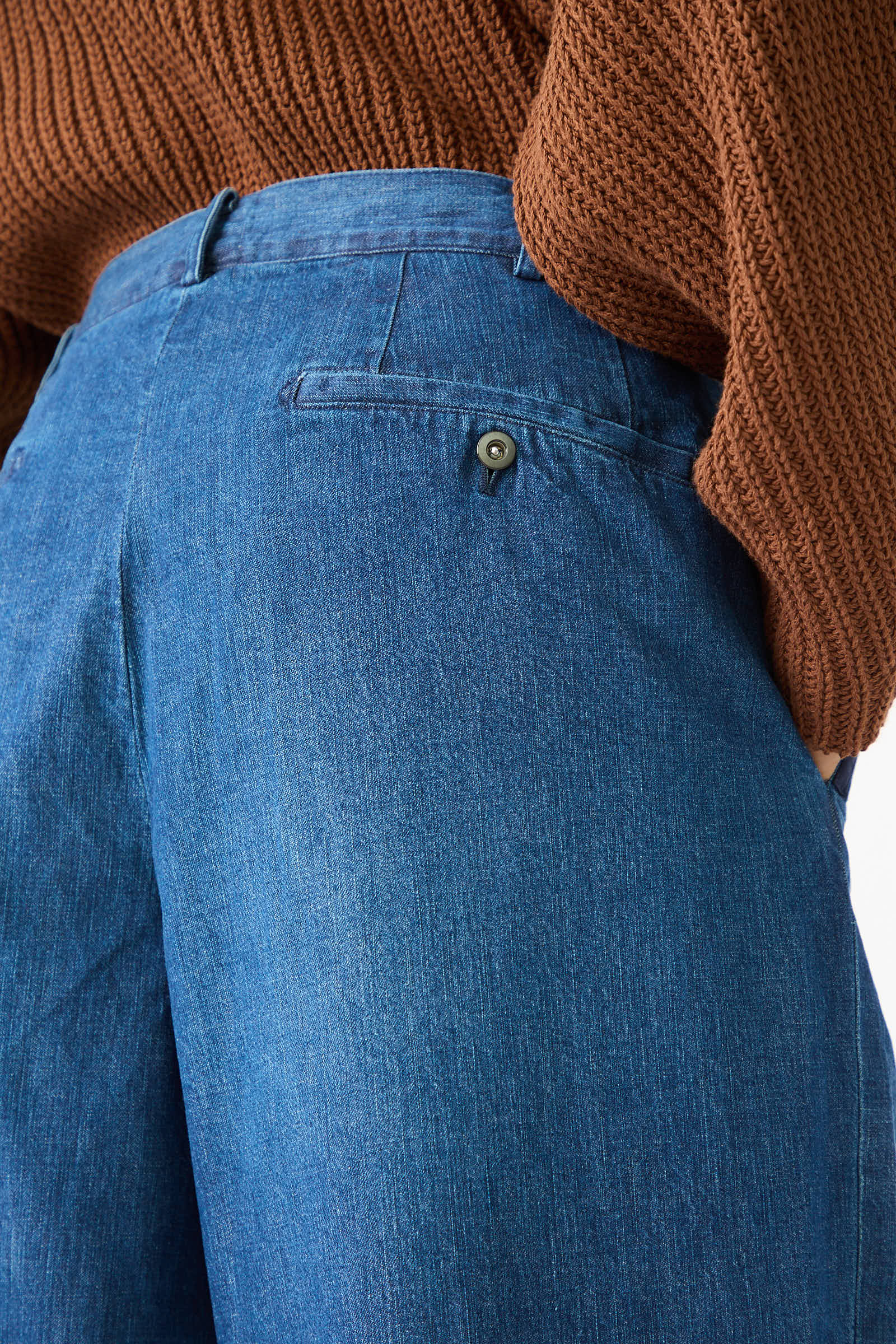 Close-up of a person wearing Chimala's 8oz. Denim Trouser in Indigo with a buttoned back pocket and a brown knit sweater.