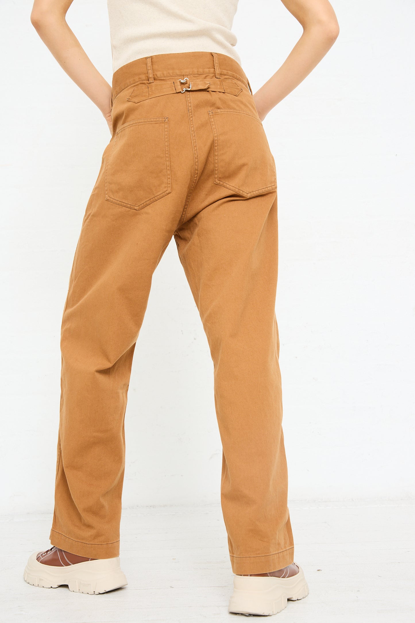 Rear view of a person wearing brown Chimala Classic Drill US Army Work Trouser in Camel standing with hands on hips.