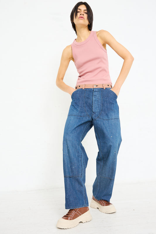 A person standing confidently with hands on hips, wearing a pink sleeveless top, oversized Chimala Denim Double Knee Work Pant in Indigo jeans, and chunky sole shoes.