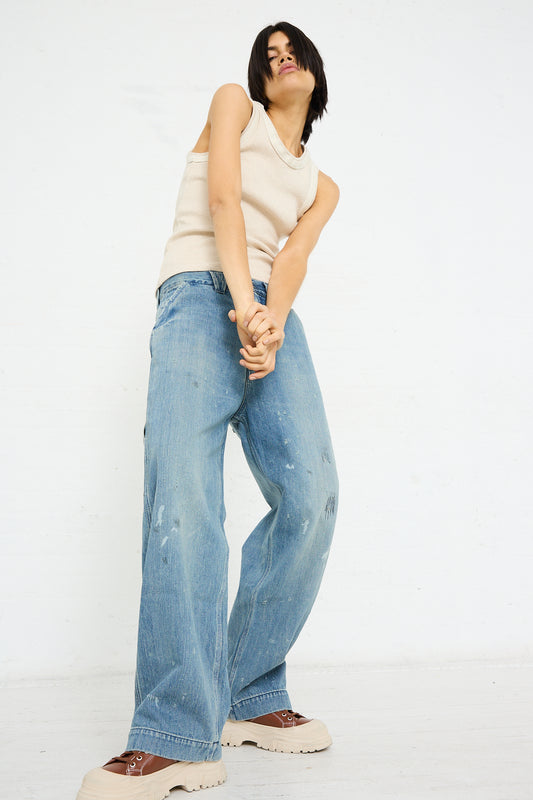 A person in a sleeveless top and wide-leg selvedge Chimala jeans standing against a white background.
