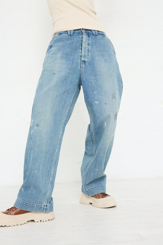 Person standing sideways wearing distressed, selvedge Chimala denim blue jeans and brown shoes.