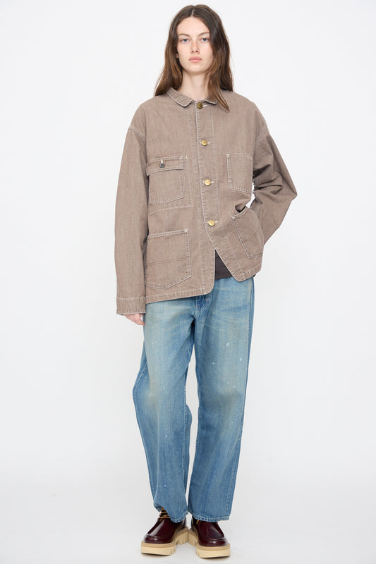 Person standing against a white background wearing the Chimala Denim Short Chore Jacket in Brown, relaxed fit blue jeans, and brown shoes.