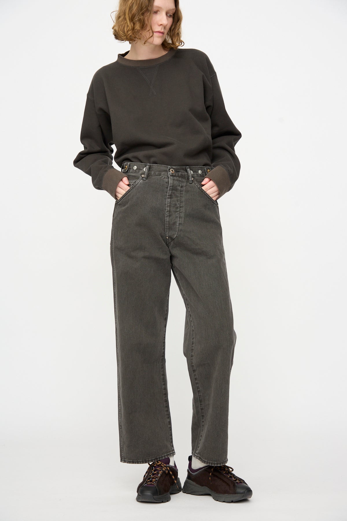 A person wearing a loose dark sweater, Chimala Rope Dyed Twill Adjustable Pant in Charcoal, and black sneakers stands with hands in pockets against a plain white background.