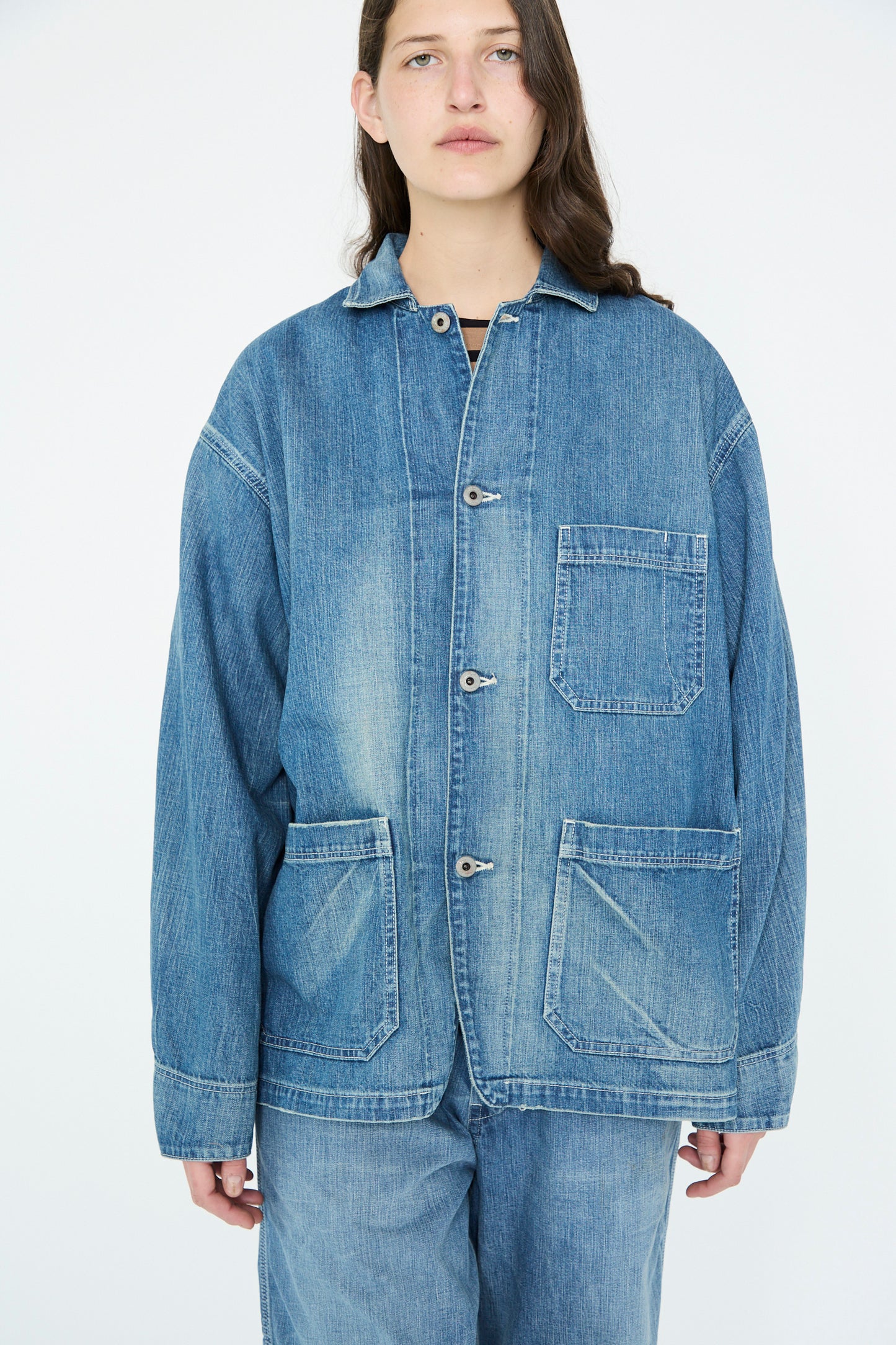 A person wearing a Chimala Selvedge Denim Chore Jacket in Medium Vintage with matching pants poses against a plain white backdrop.