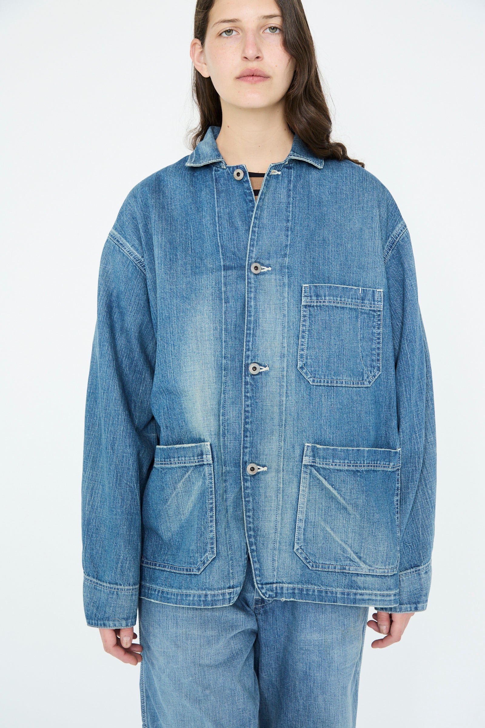 A person wearing a Chimala Selvedge Denim Chore Jacket in Medium Vintage with matching pants poses against a plain white backdrop.