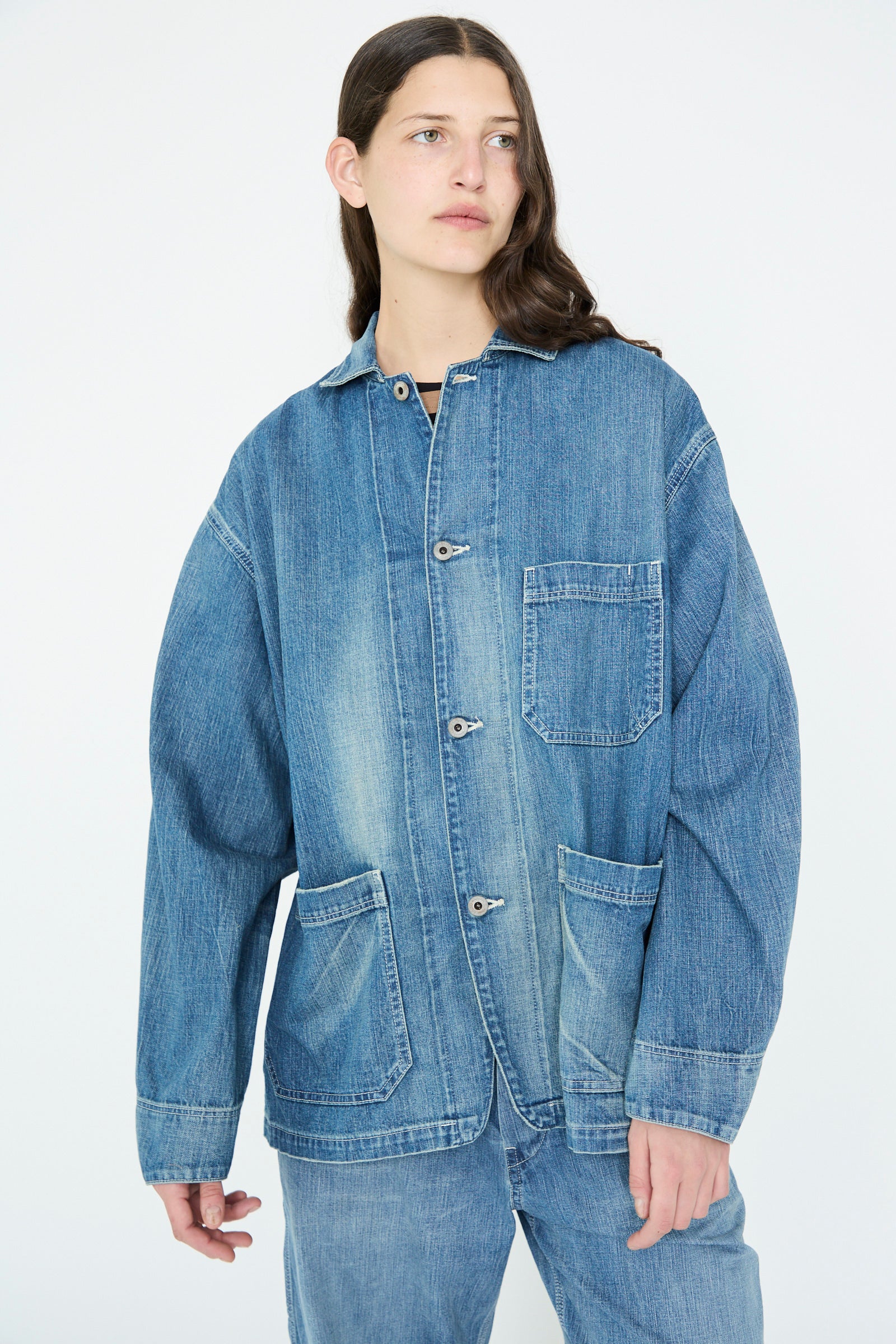 A person with long hair models the Chimala Selvedge Denim Chore Jacket in Medium Vintage against a plain background, wearing jeans.