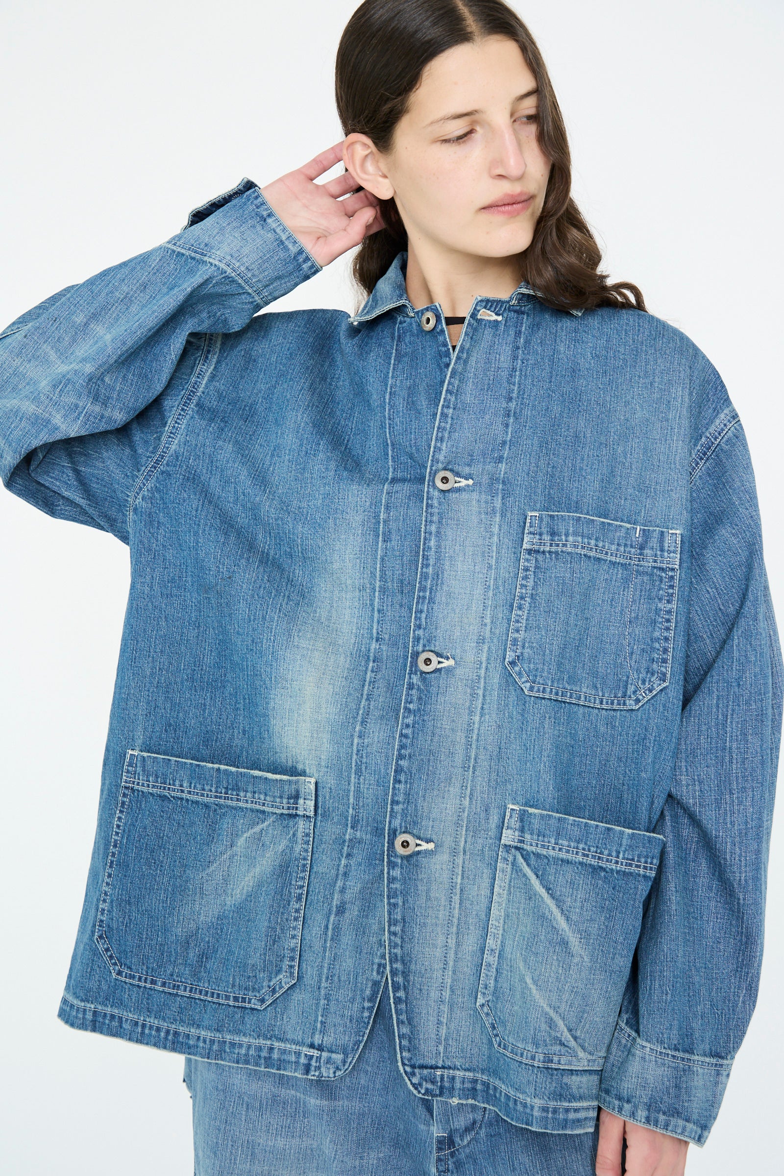 A person in a Chimala Selvedge Denim Chore Jacket in Medium Vintage gazes to the side with a relaxed expression against a neutral background.