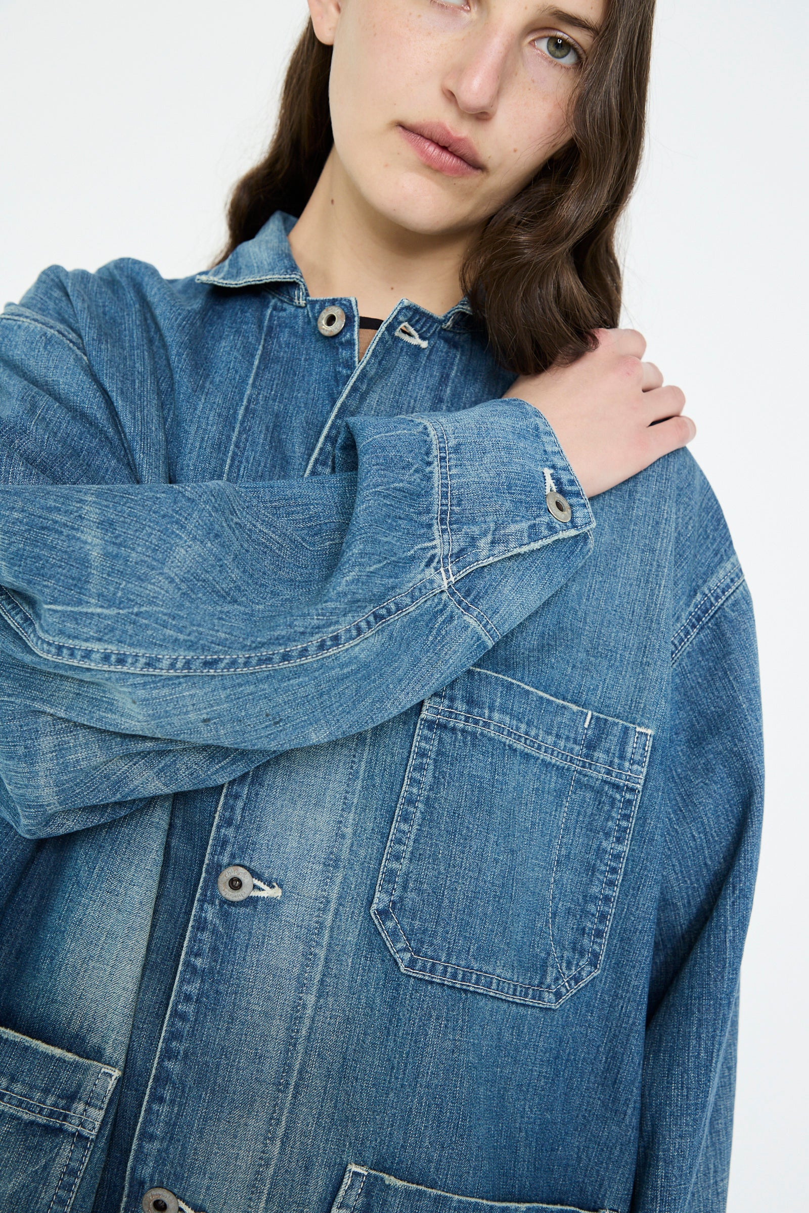 A person wearing a Chimala Selvedge Denim Chore Jacket in Medium Vintage stands against a plain background.