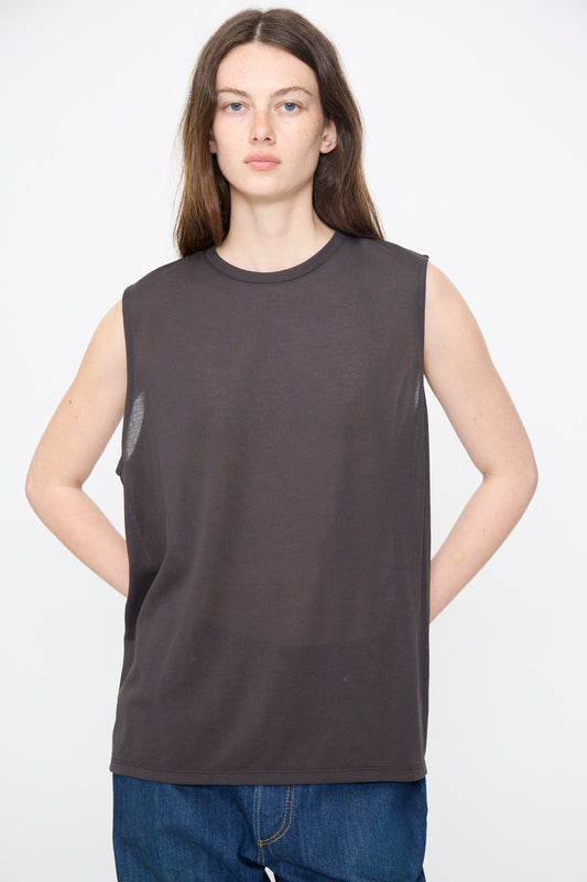 A person with long brown hair wears the Chimala Sheer Fleece Muscle Tee in Charcoal and blue jeans, standing against a plain white background.