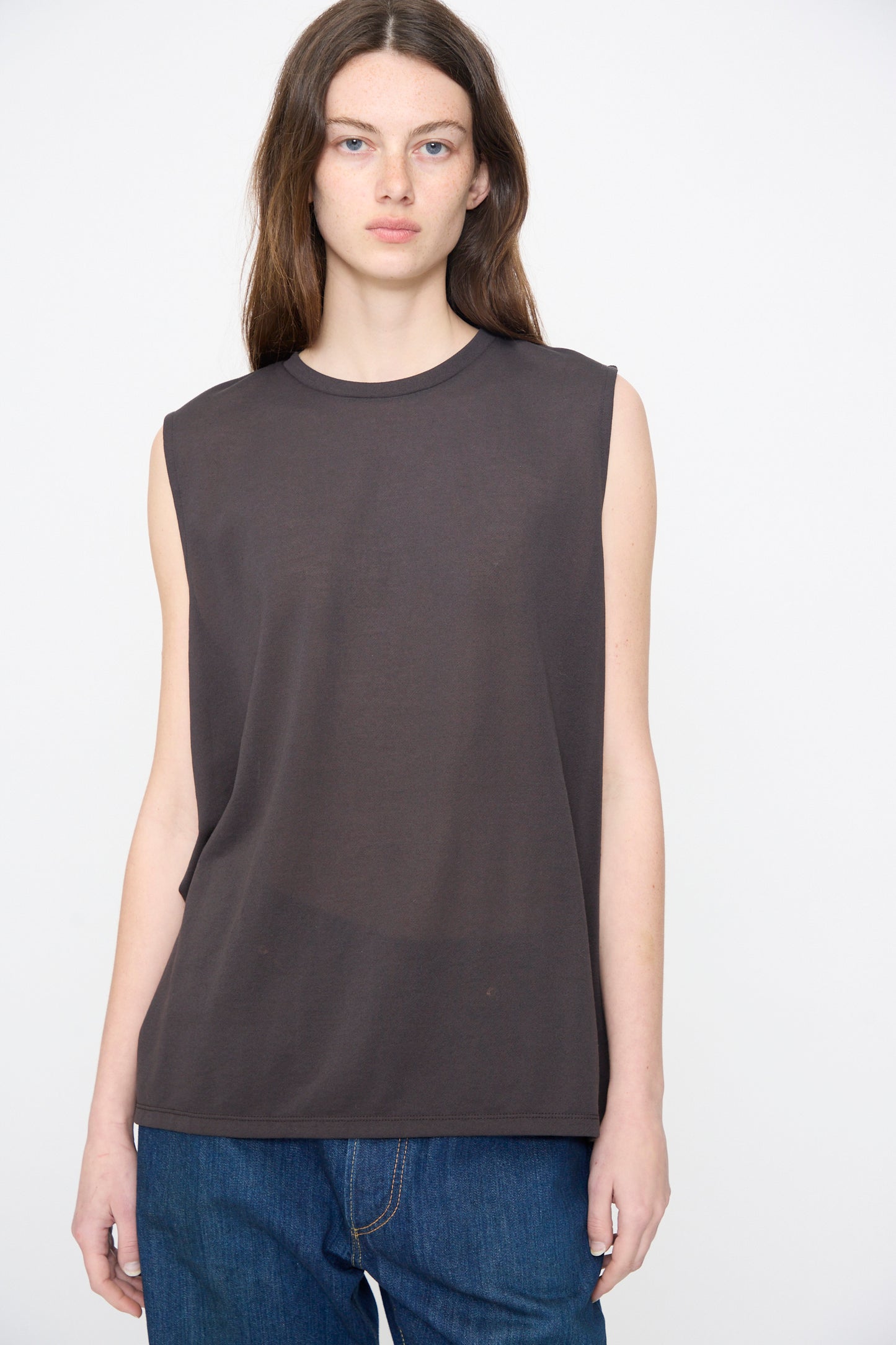 A person wears the Chimala Sheer Fleece Muscle Tee in Charcoal with blue jeans, standing against a plain white background.