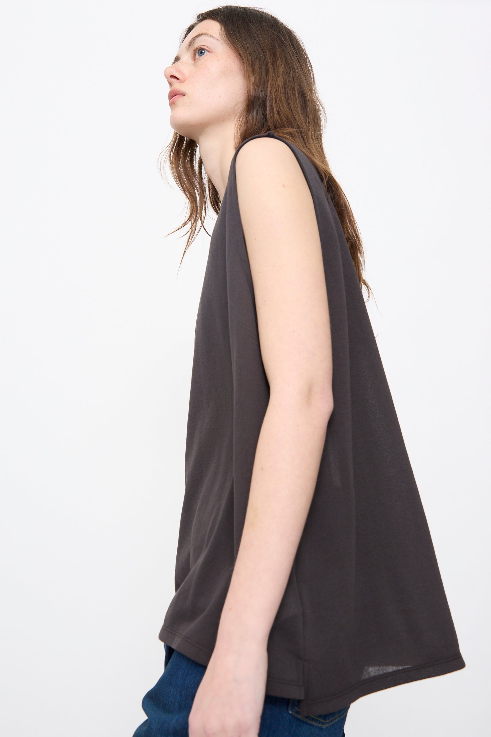 Person with long brown hair wears the Chimala Sheer Fleece Muscle Tee in Charcoal and blue jeans, standing against a plain white background.