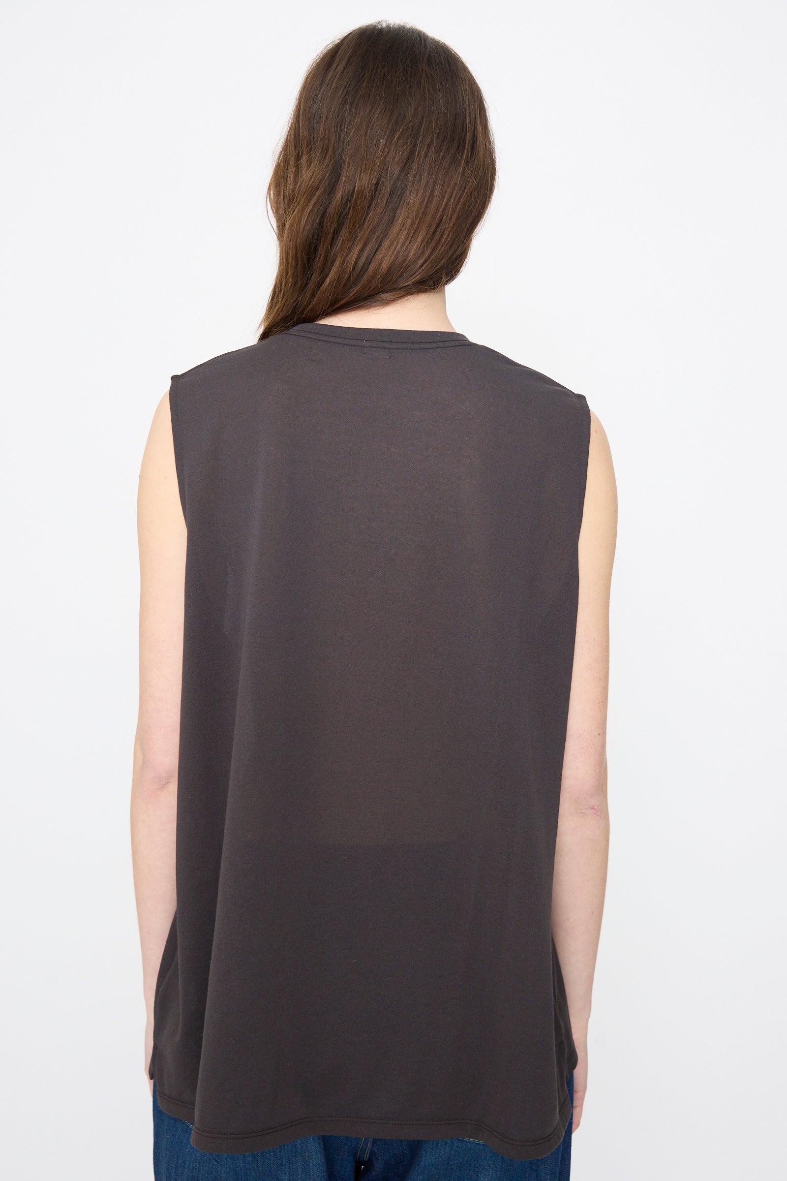 Person with long brown hair shown from the back, wearing Chimala's Sheer Fleece Muscle Tee in Charcoal—a relaxed fit sleeveless top—paired with blue jeans, set against a plain white background.