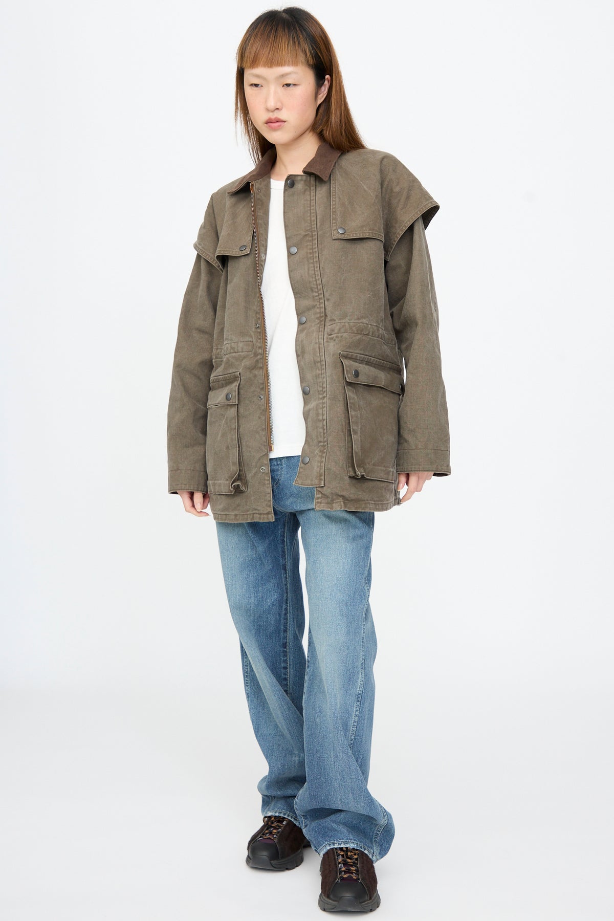 A model wears a brown Chimala Sulfer Dyed Canvas Lumber Coat with a suede collar, deep front pockets, and a wide back yoke over a white t-shirt and blue jeans.