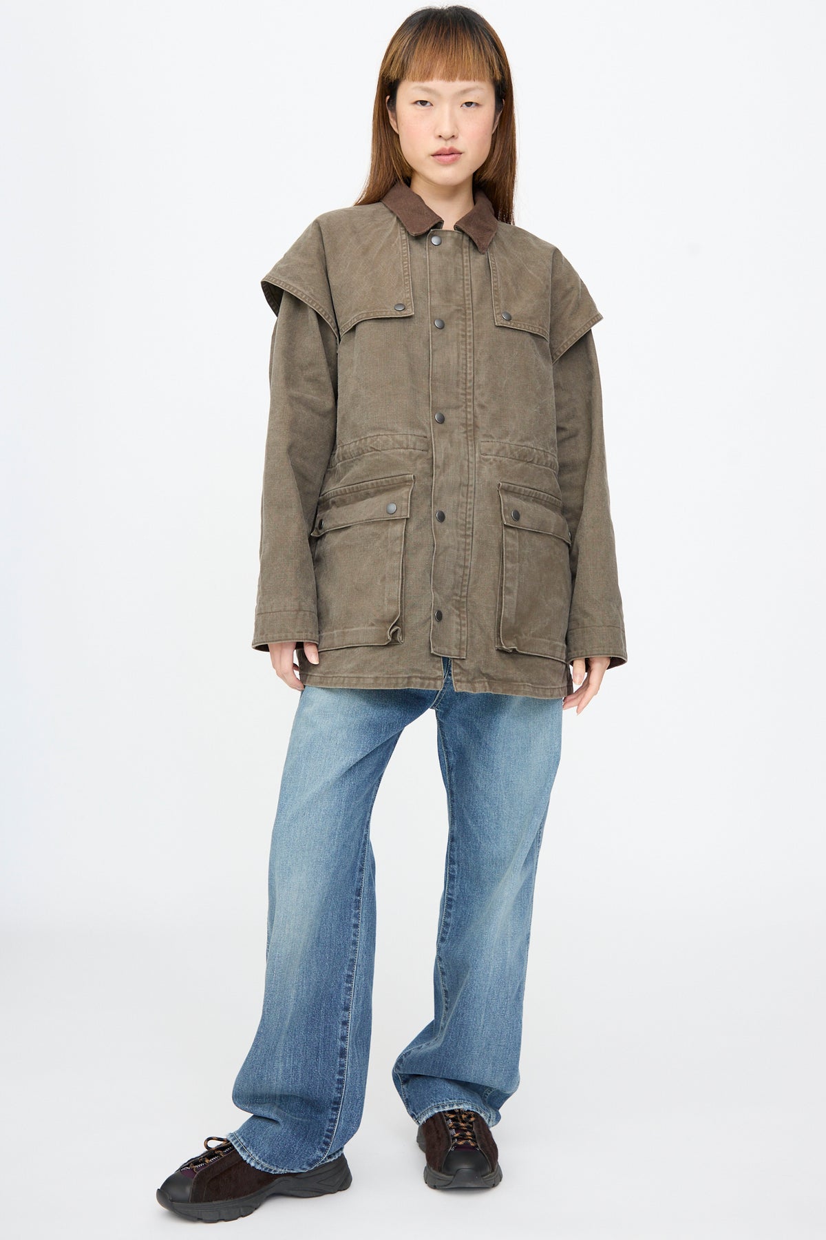 A person wearing a Chimala Sulfer Dyed Canvas Lumber Coat in Brown with a suede collar and large front pockets over blue jeans.
