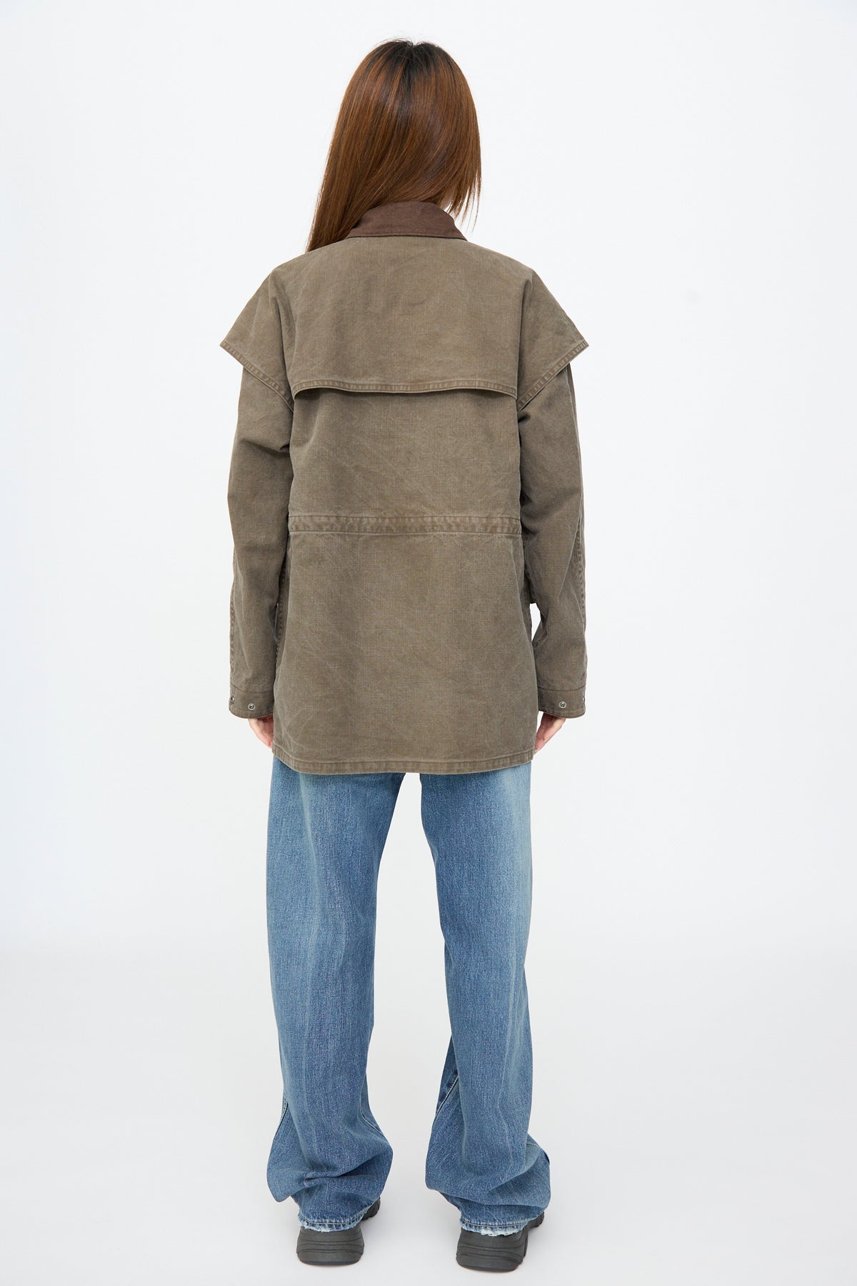 Person wearing a brown Chimala Sulfer Dyed Canvas Lumber Coat with a suede collar and large back panel, paired with blue jeans.