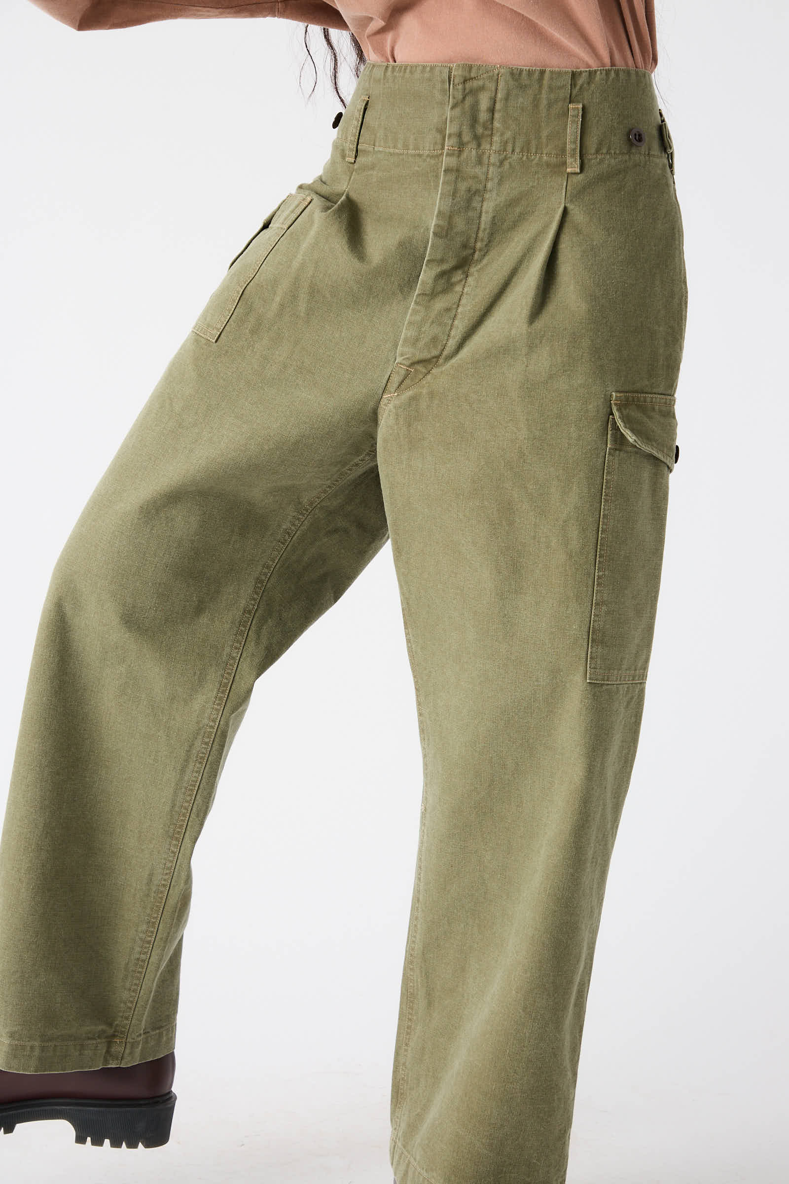 Person wearing the Chimala Unisex Belgian Waist Gathering Cargo Pant in Olive and black shoes. Upper body is partially visible, wearing a peach-colored top.