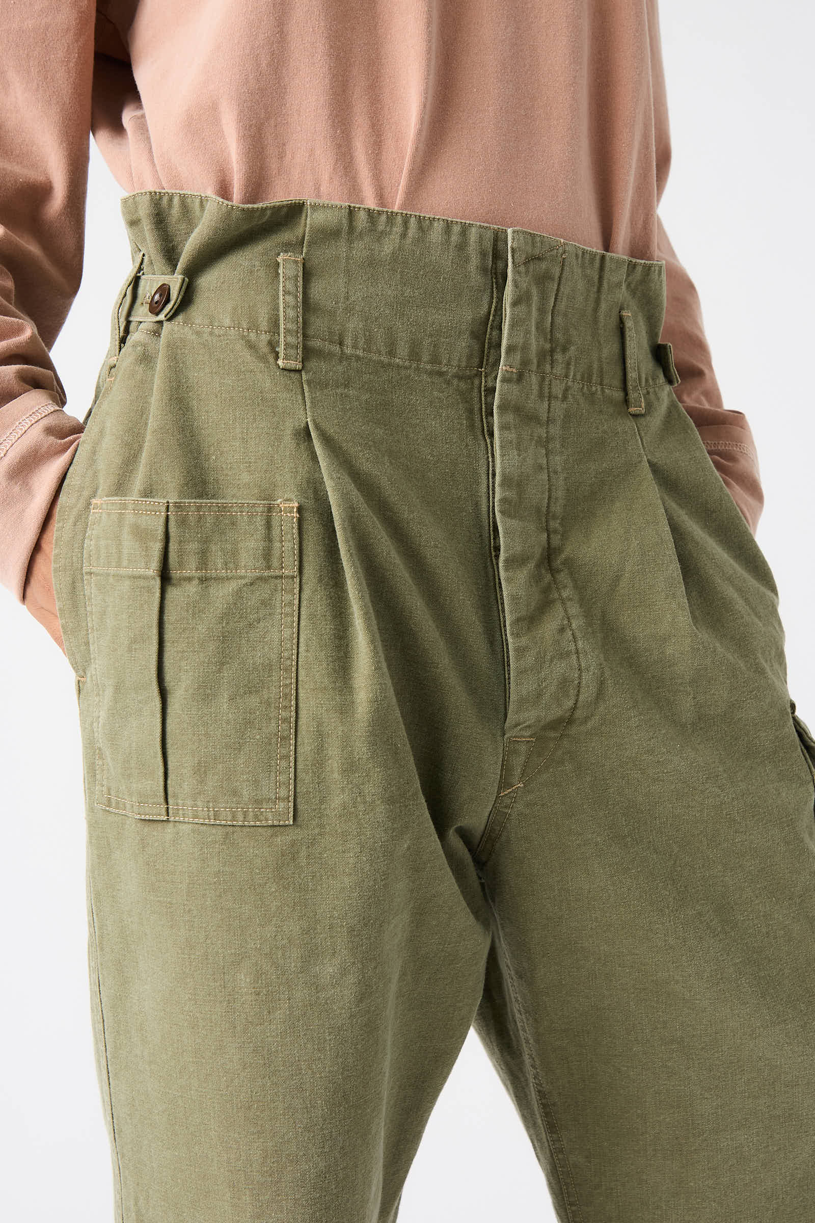 A person wearing the Chimala Unisex Belgian Waist Gathering Cargo Pant in Olive, which features high-waisted, multiple pockets and is made from sulfur-dyed canvas, paired with a beige top.