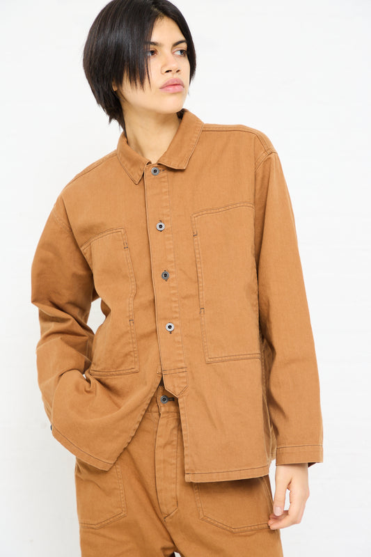 A person in a Chimala Unisex Classic Drill US Army Work Jacket in Camel and matching pants, looking to the side against a white background.