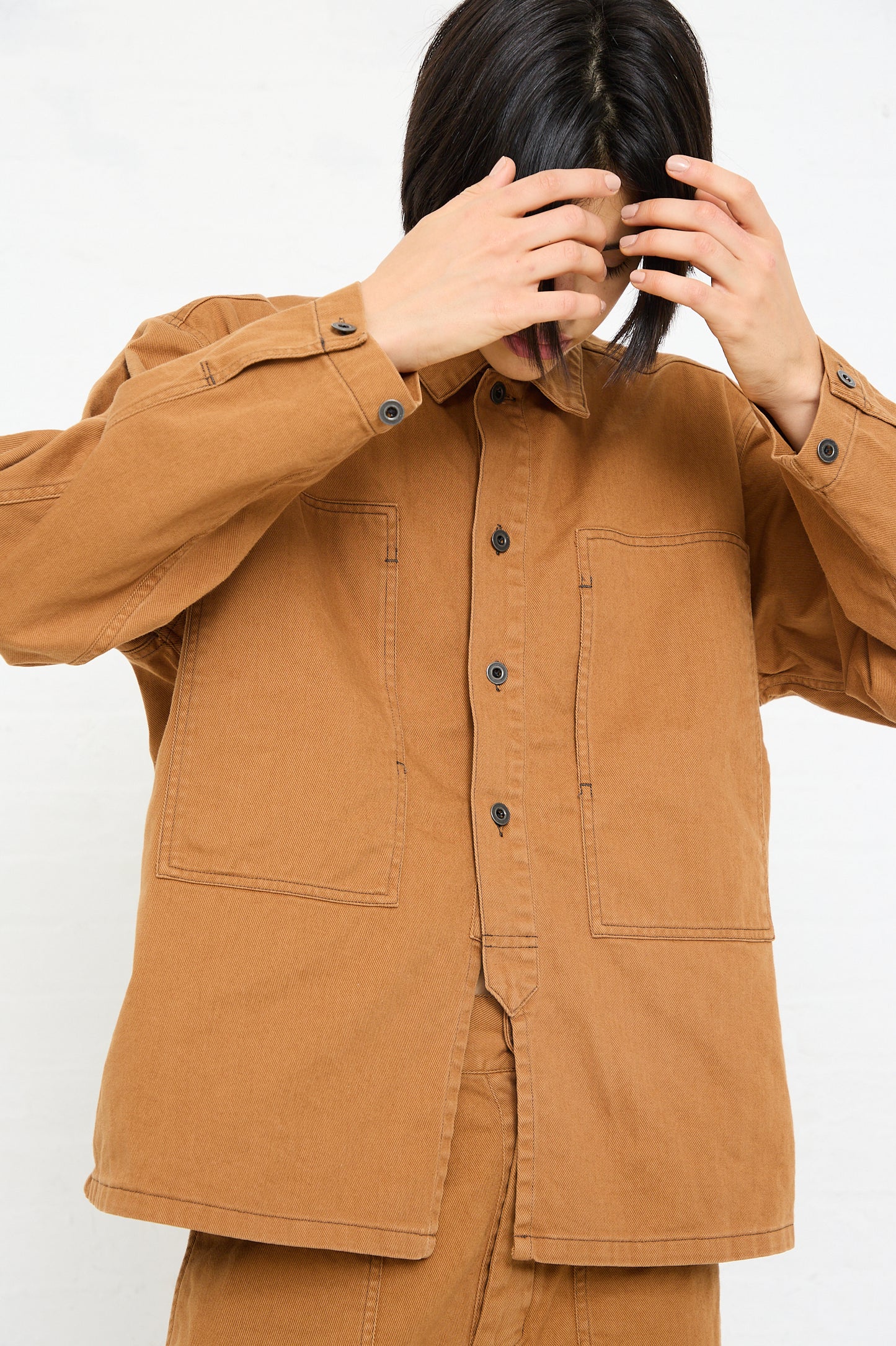 A person in a Chimala Unisex Classic Drill US Army Work Jacket in Camel covering their face with their hands.