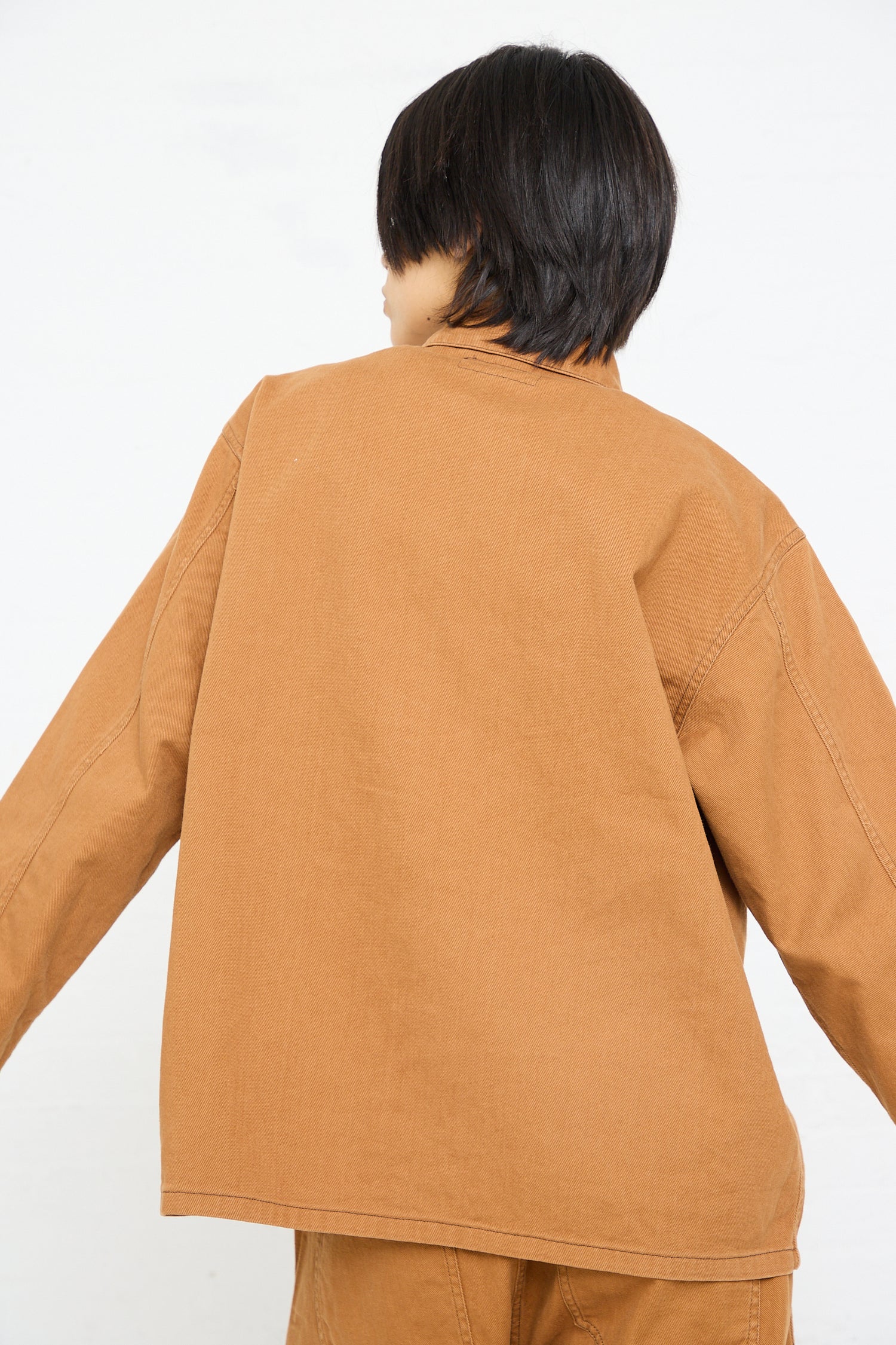 Person wearing a Chimala Unisex Classic Drill US Army Work Jacket in Camel from behind against a white background.