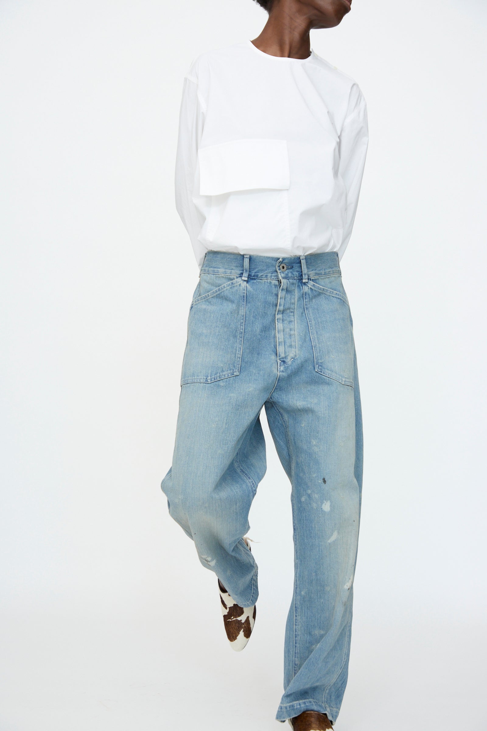 A person wearing a white long-sleeve shirt, Chimala Unisex US Army Style Denim Trouser in Light Vintage, and brown patterned shoes stands against a plain white background.