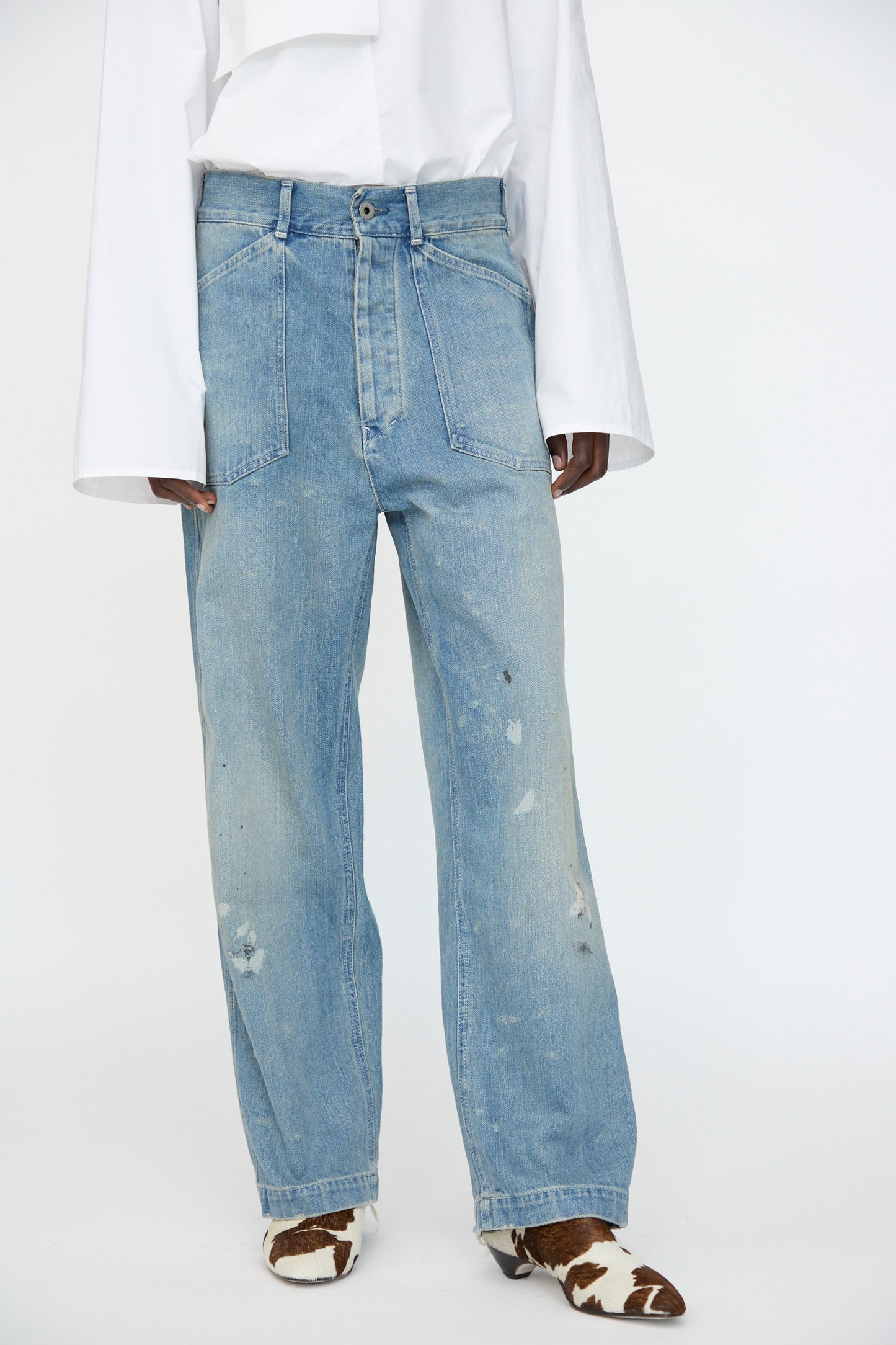 A person wears a white long-sleeve shirt, Chimala Unisex US Army Style Denim Trouser in Light Vintage, and cow-print shoes, standing against a plain white background.