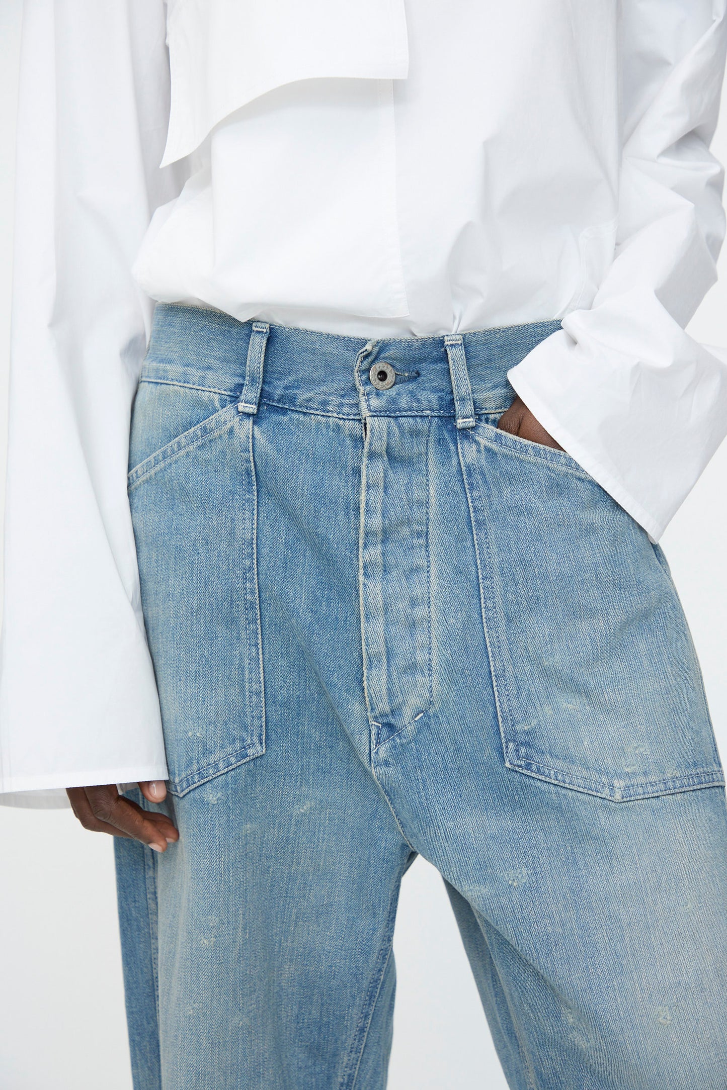 Model wears Chimala's Unisex US Army Style Denim Trouser in Light Vintage—relaxed fit with unique front panel details—and a white long-sleeve shirt, hand in pocket.