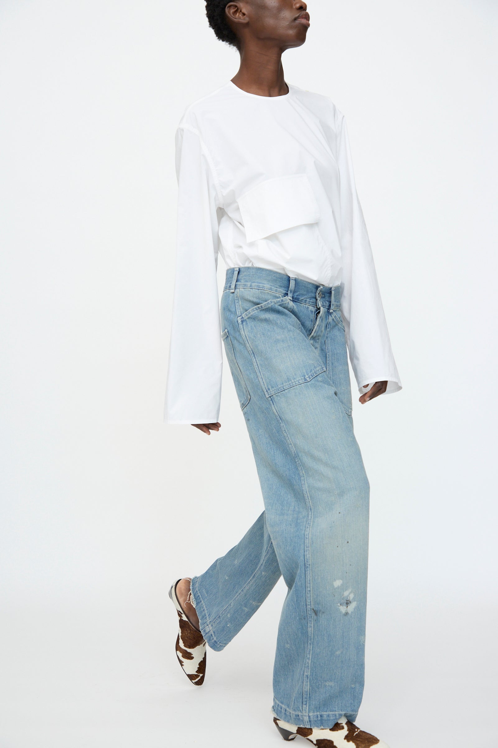 Person wearing a long-sleeve white shirt with a large chest pocket, Chimala Unisex US Army Style Denim Trouser in Light Vintage, and brown-and-white shoes, standing against a plain white background.