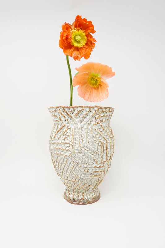 The Ridge Vase in Brown by Claire Resnick Ceramics, a textured hand-built ceramic piece, holds two poppy flowers—one orange and one pale peach—set against a plain white background.