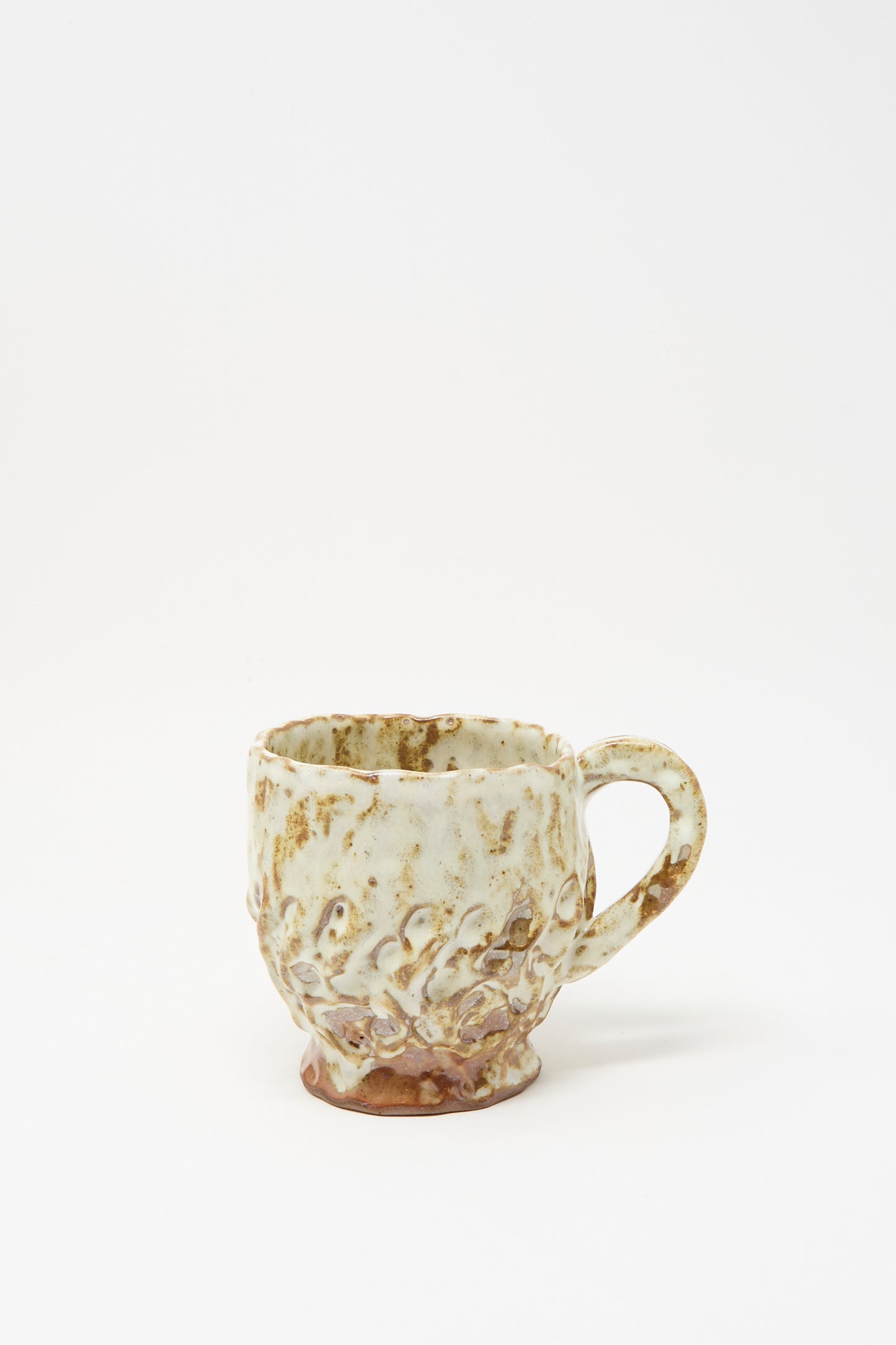 The Textured Mug in White Brown Mix I by Claire Resnick Ceramics is a handmade, hand-built ceramic mug featuring a wavy, textured surface and a speckled glaze in beige and brown tones. Shown against a plain white background, this unique mug is proudly made in the USA.