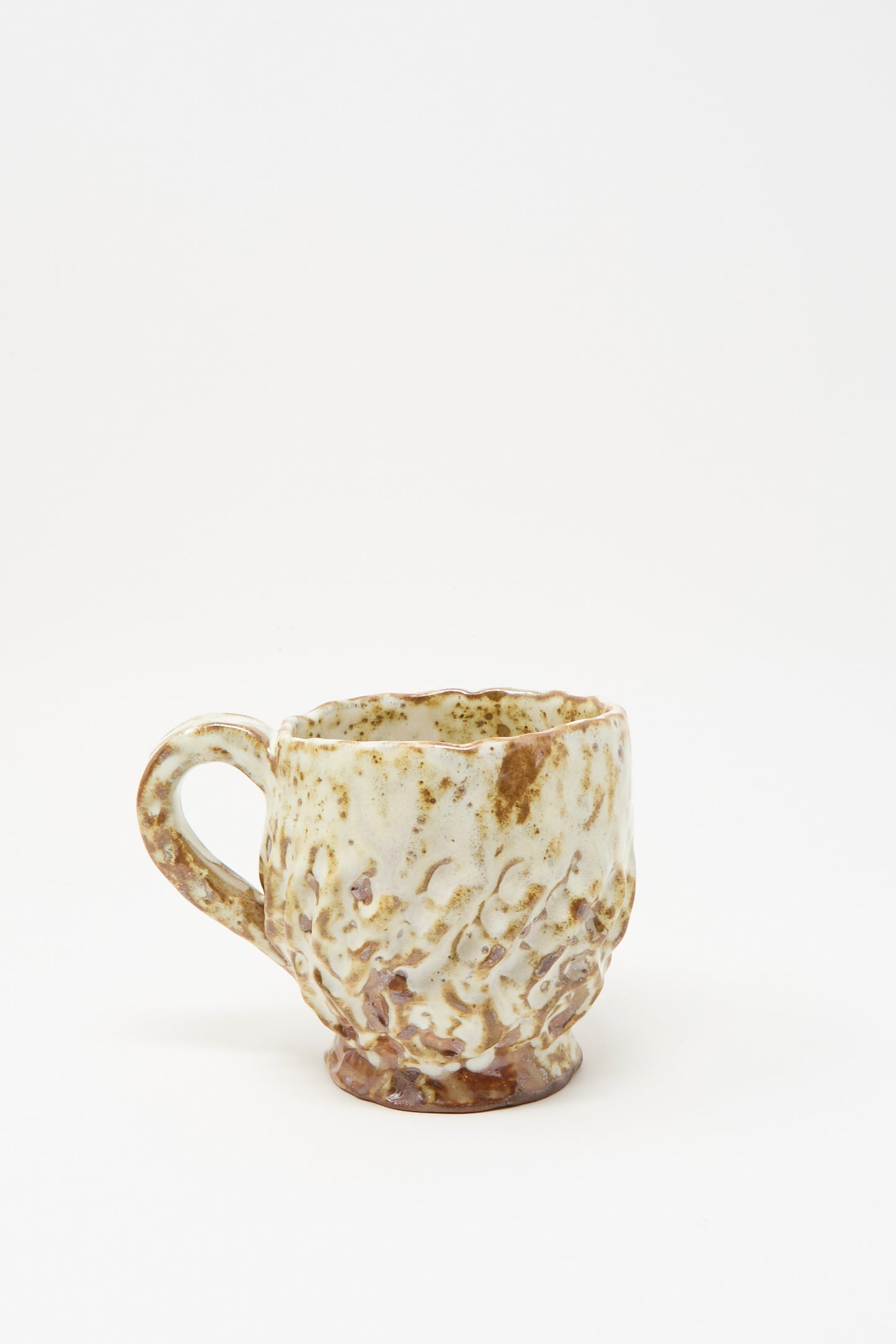 The Claire Resnick Ceramics Textured Mug in White Brown Mix I is displayed against a plain white background, featuring a handmade, dimpled ceramic surface with a blend of cream and brown glaze. Crafted in the USA, this unique hand-built mug highlights exceptional craftsmanship and distinctive style.