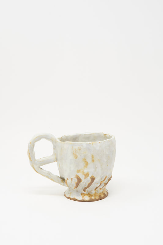 The Textured Mug in White Mix by Claire Resnick Ceramics is a hand-built ceramic mug showcasing a rough texture, an irregular shape, and a twisted handle. Featuring a white glaze with brown accents, this unique piece is made in the USA and displayed against a plain white background.