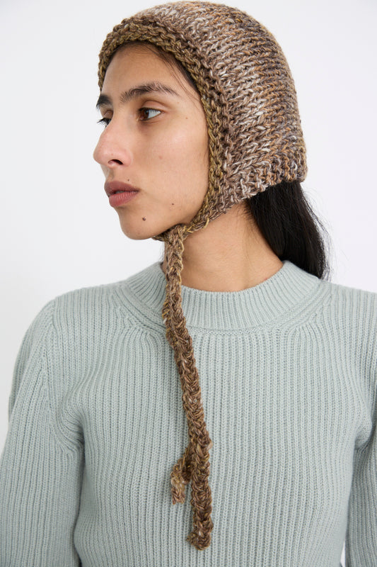 A person wearing a gray knit sweater and Clyde's Knit Wool Space Bonnet in Venus Brown, featuring Japanese yarn and brown crochet chin ties, is looking to the side against a plain background.