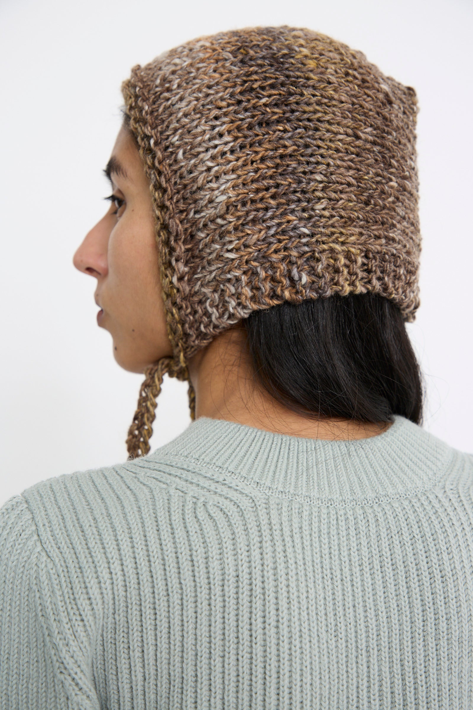 A person is seen from the back looking to the left, wearing the Clyde Knit Wool Space Bonnet in Venus Brown, made from Japanese yarn.