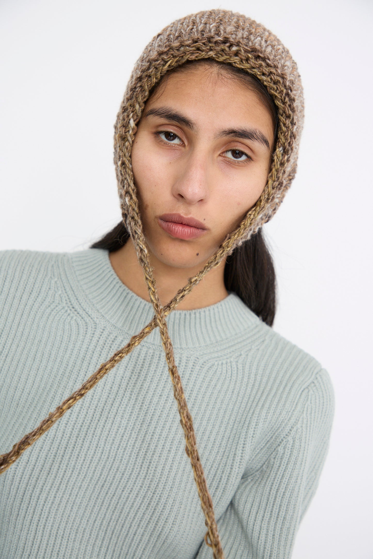 A person wearing the Clyde Knit Wool Space Bonnet in Venus Brown and a light gray sweater, looking at the camera against a plain background.