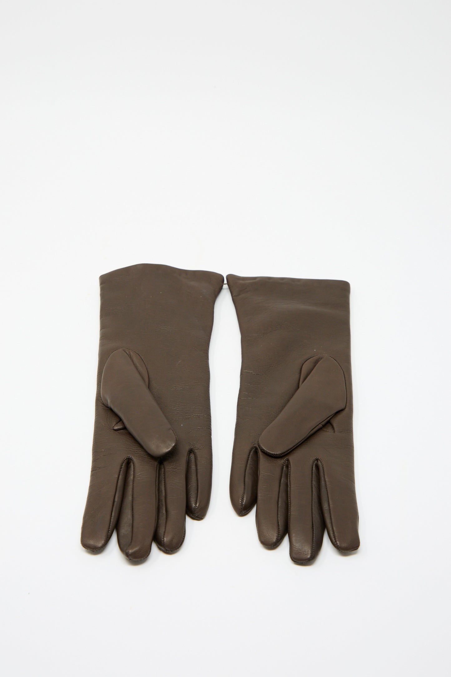 The Clyde Lambskin and Cashmere Classic Gloves in Espresso rest on a white surface. Made in Italy, these exquisitely crafted gloves feature a cashmere lining for unparalleled comfort and warmth.