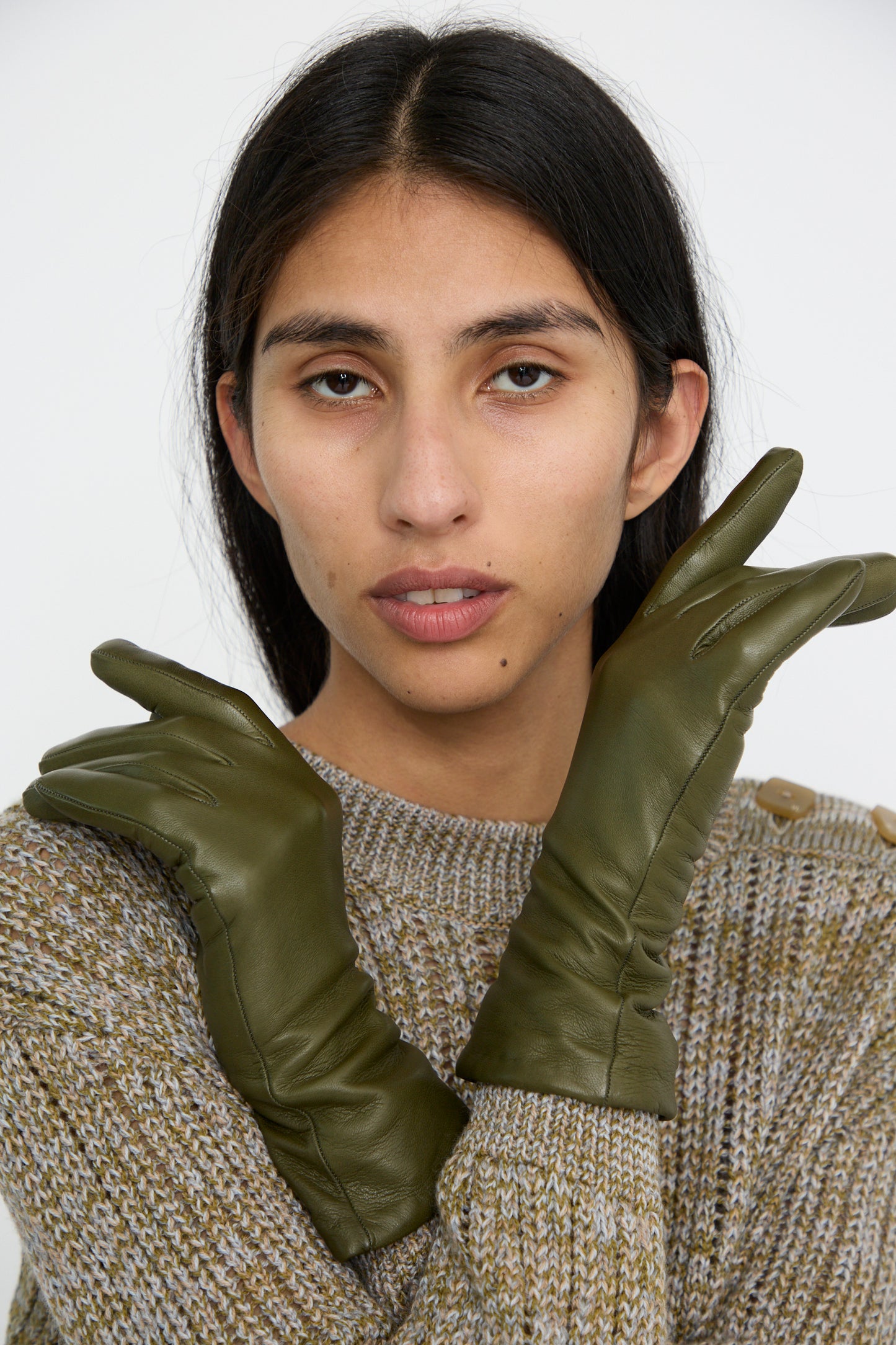 A person wearing Clyde’s Lambskin and Cashmere Classic Glove in Bog Green poses with hands crossed near their face, dressed in a green knit sweater.