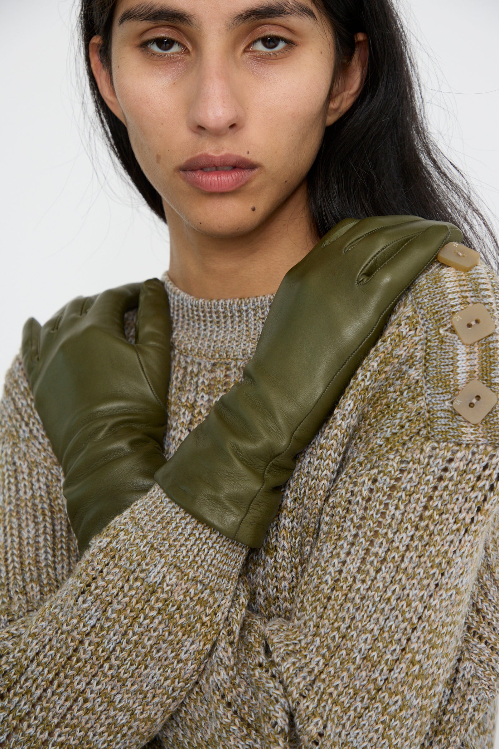 A person wearing Clyde's Lambskin and Cashmere Classic Glove in Bog Green alongside a knit sweater with button details on the shoulder.