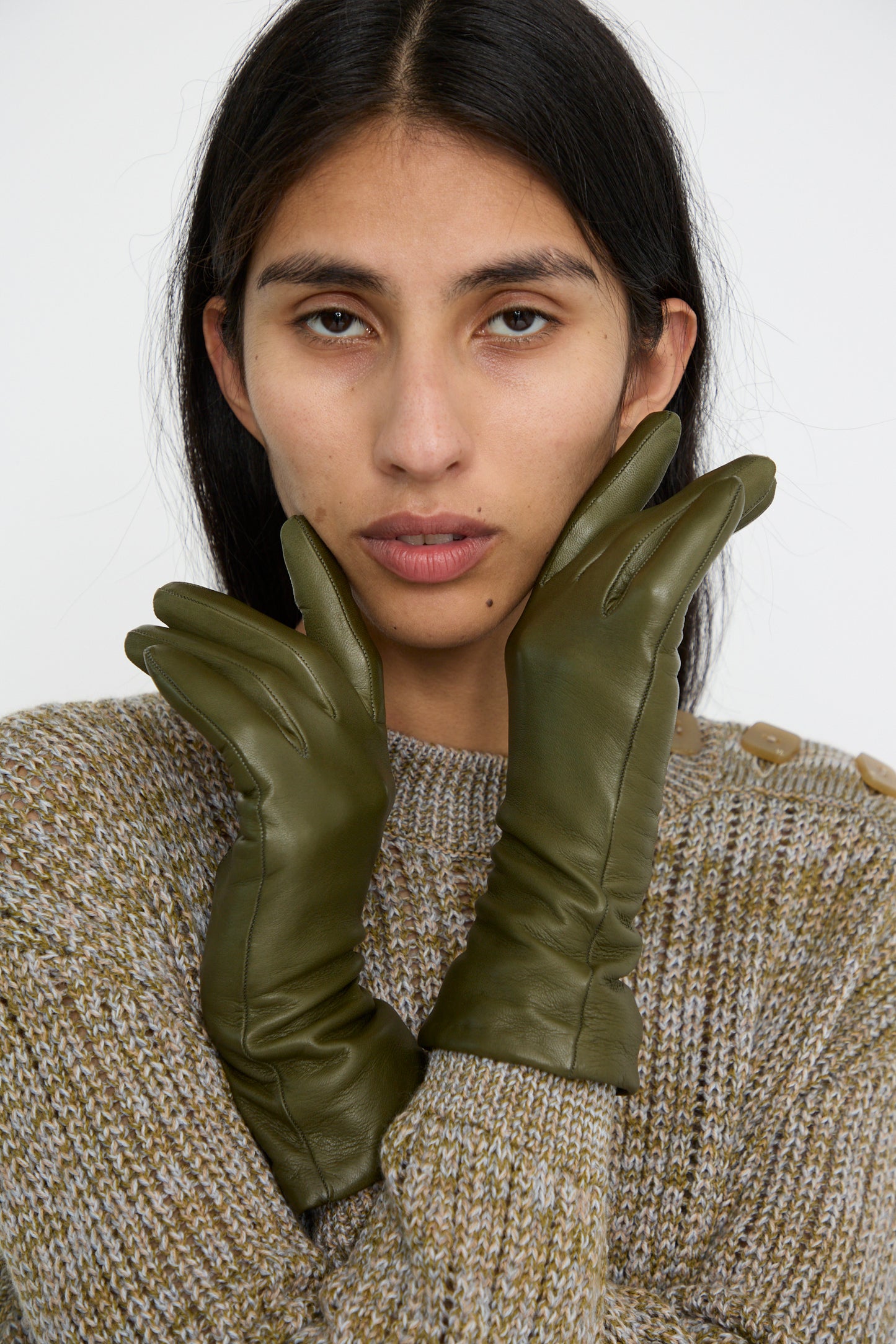 A person wearing a knit sweater and Clyde's Lambskin and Cashmere Classic Glove in Bog Green, crafted in Italy with  cashmere lining, poses with their hands near their face against a white background. 