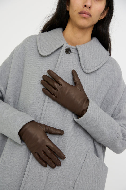 Person wearing a light gray coat with a rounded collar and Clyde's carefully crafted Lambskin and Cashmere Classic Glove in Espresso, all made in Italy.